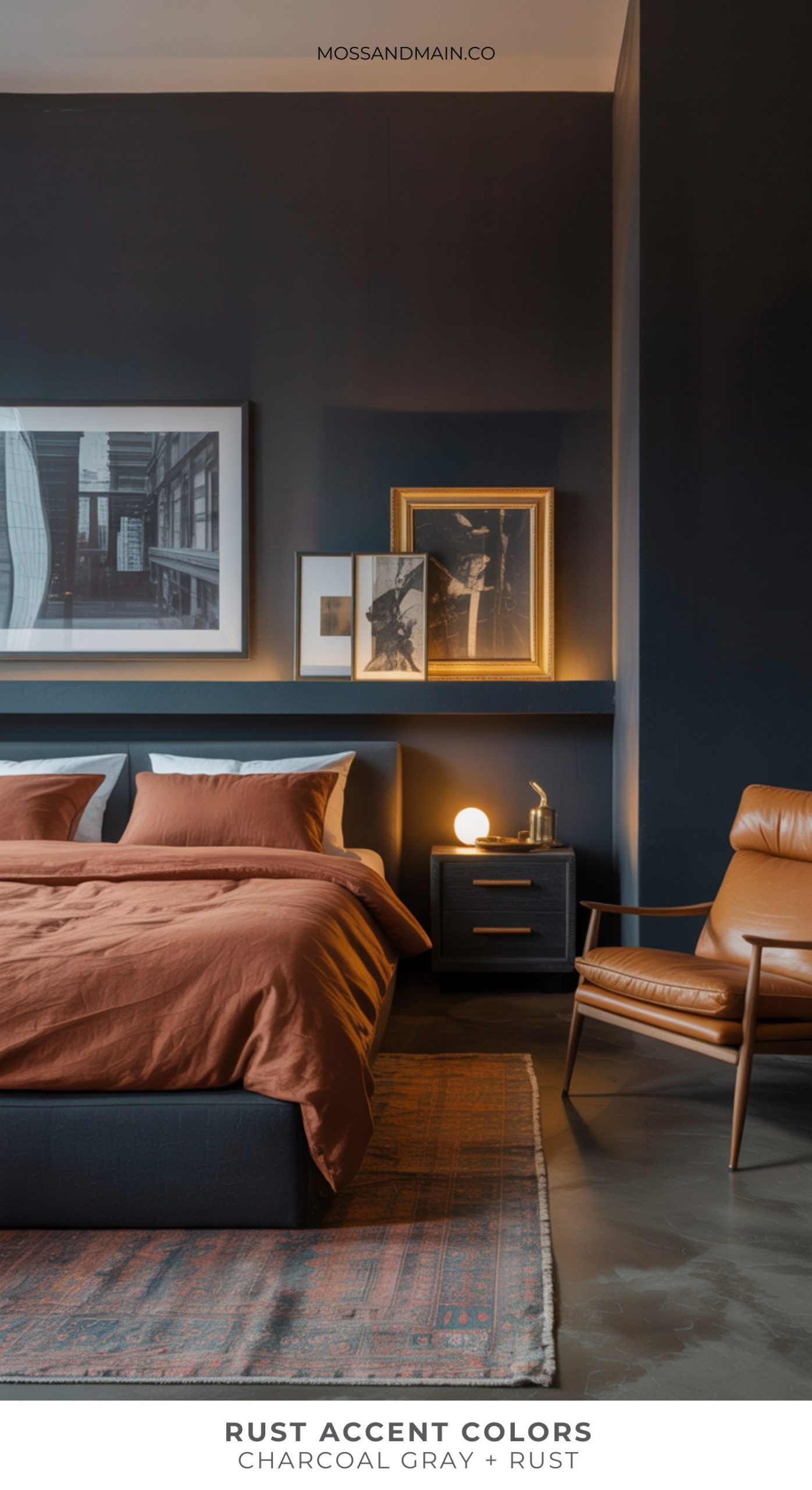 A modern bedroom with dark charcoal gray walls, rust accent colors in the bedding and matching armchair, a patterned rug, black-and-white framed art above the bed, and a nightstand with a lamp.