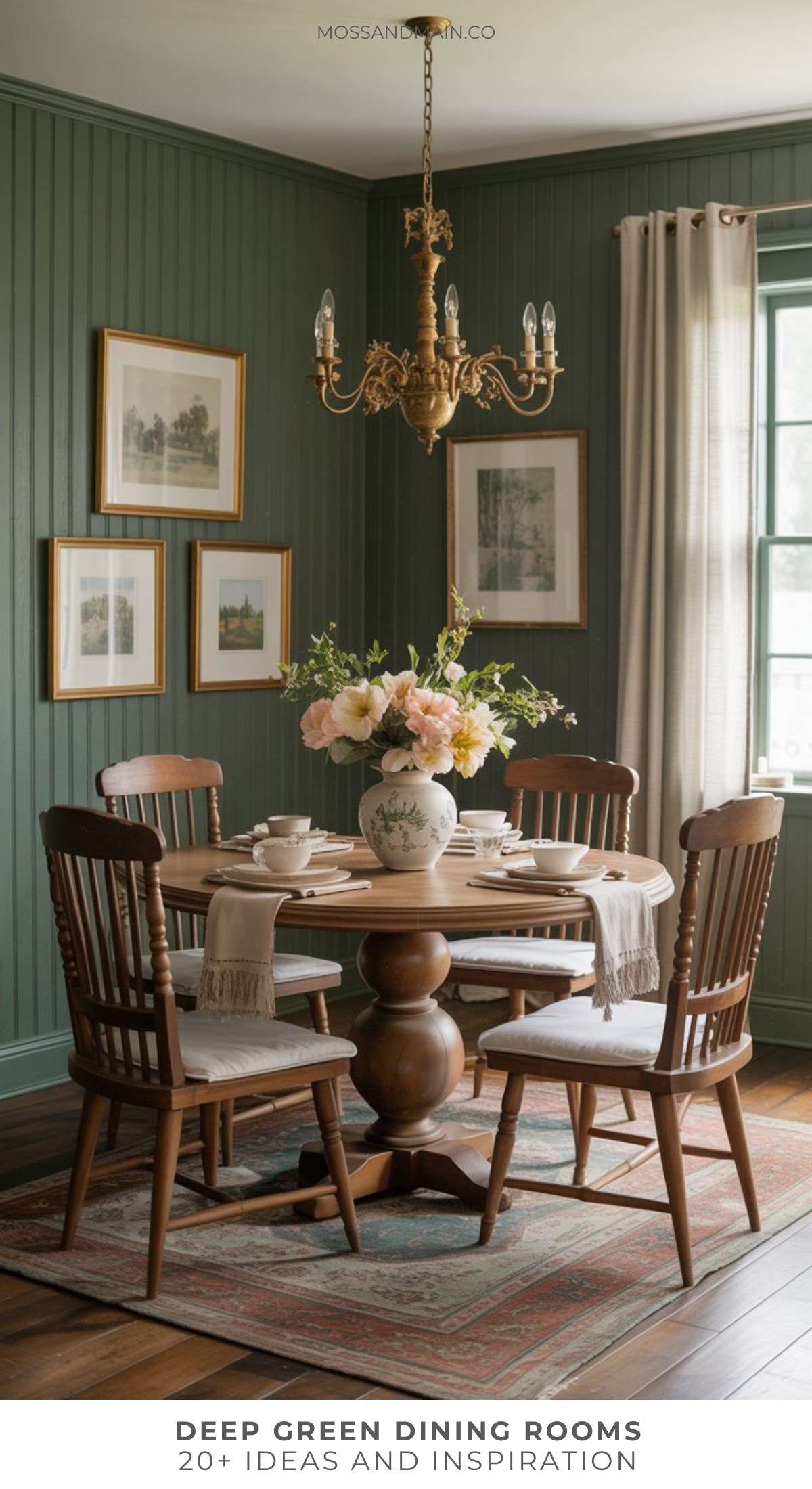 A cozy, dark green dining room features paneled walls, a wooden table and chairs, a floral centerpiece, framed artwork, a chandelier, and sunlight streaming through a window with beige curtains.