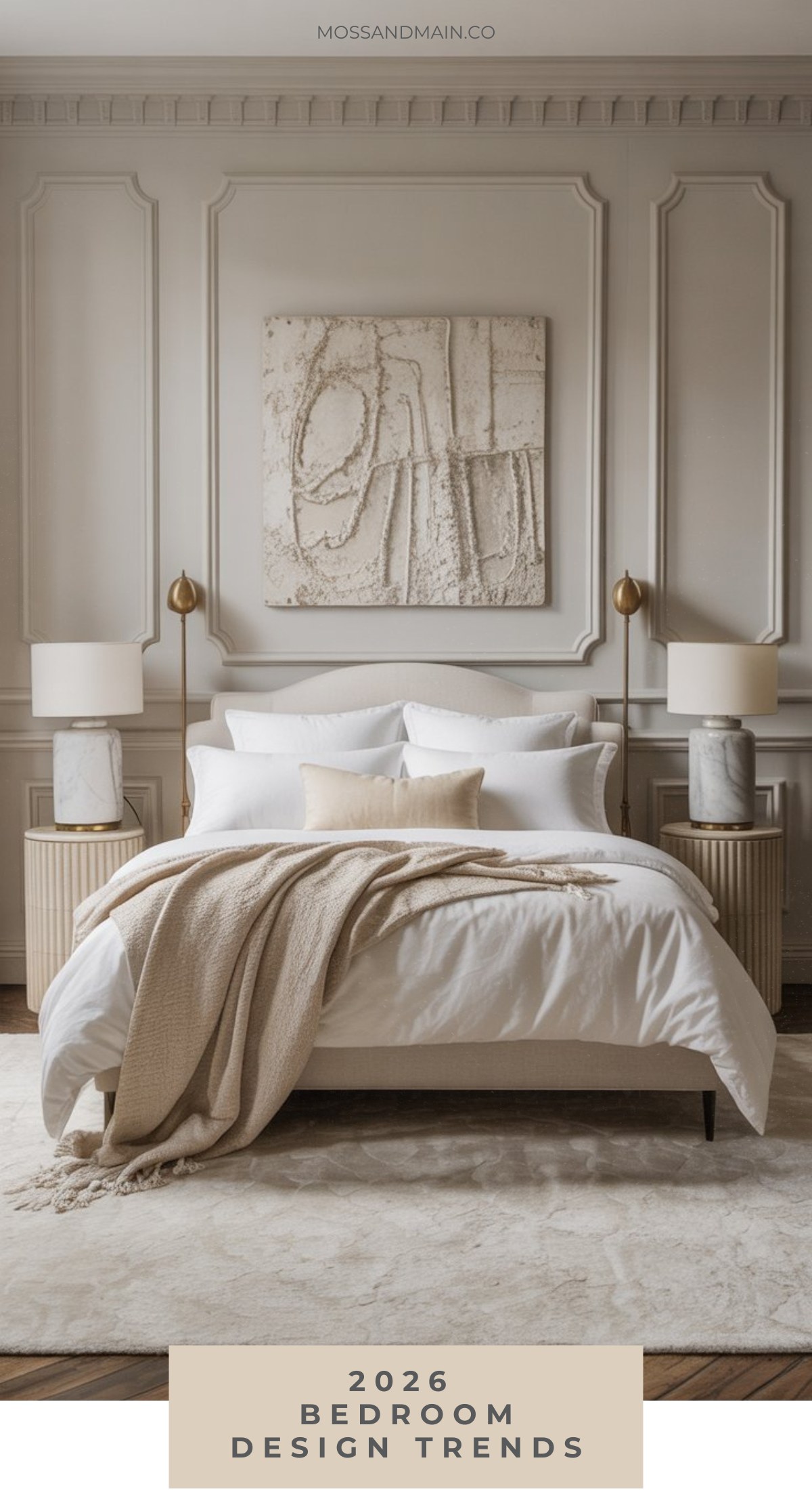 A stylish bedroom embraces the latest bedroom design trends with a neatly made bed, white bedding, beige throw, matching nightstands, and gold lamps, all set against an elegant paneled wall adorned with abstract art above the headboard.