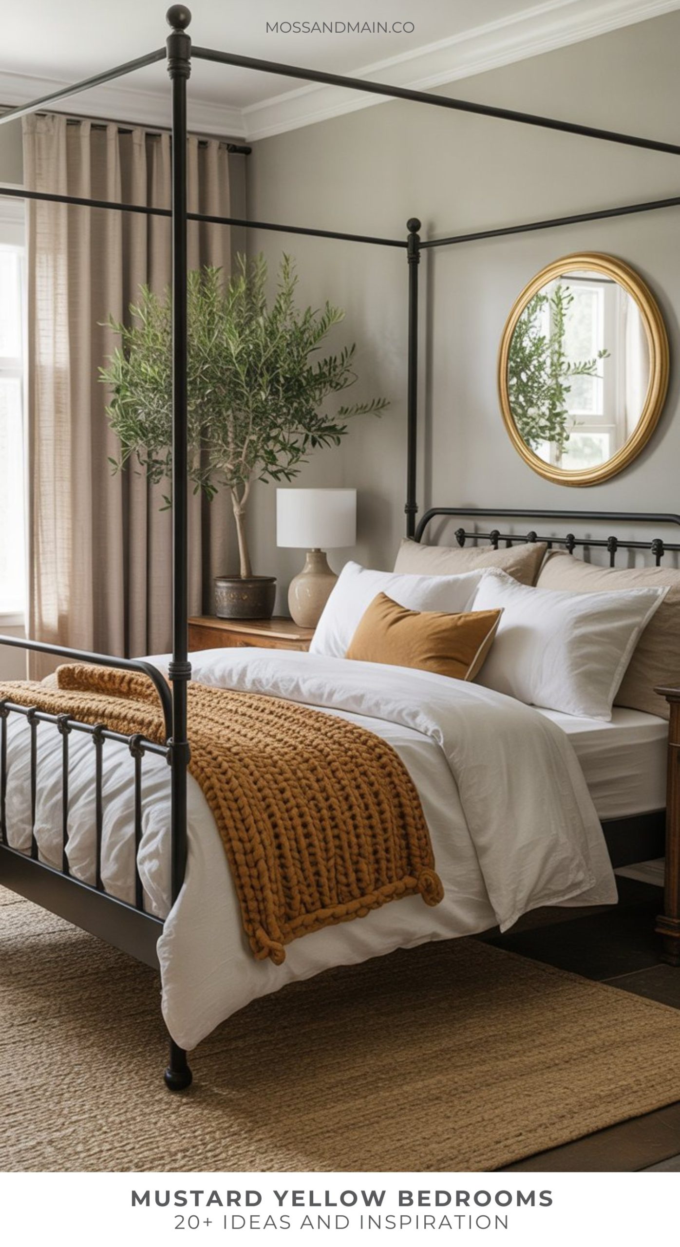A cozy bedroom decor idea with a black four-poster bed, white bedding, and mustard yellow accents. A chunky knit throw and pillow add warmth. An oval mirror and potted tree decorate the space as natural light fills the room.