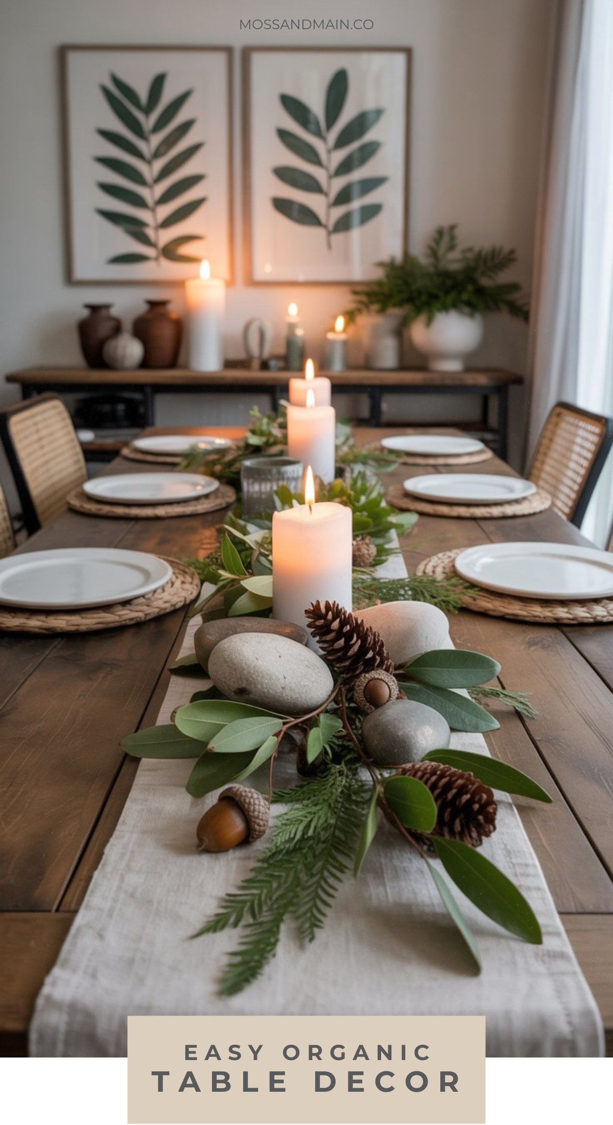 A dining table decorated with greenery, pinecones, smooth stones, acorns, and pillar candles creates an organic chic centerpiece. Wicker placemats and framed botanical prints add to this inviting dining room table decor.