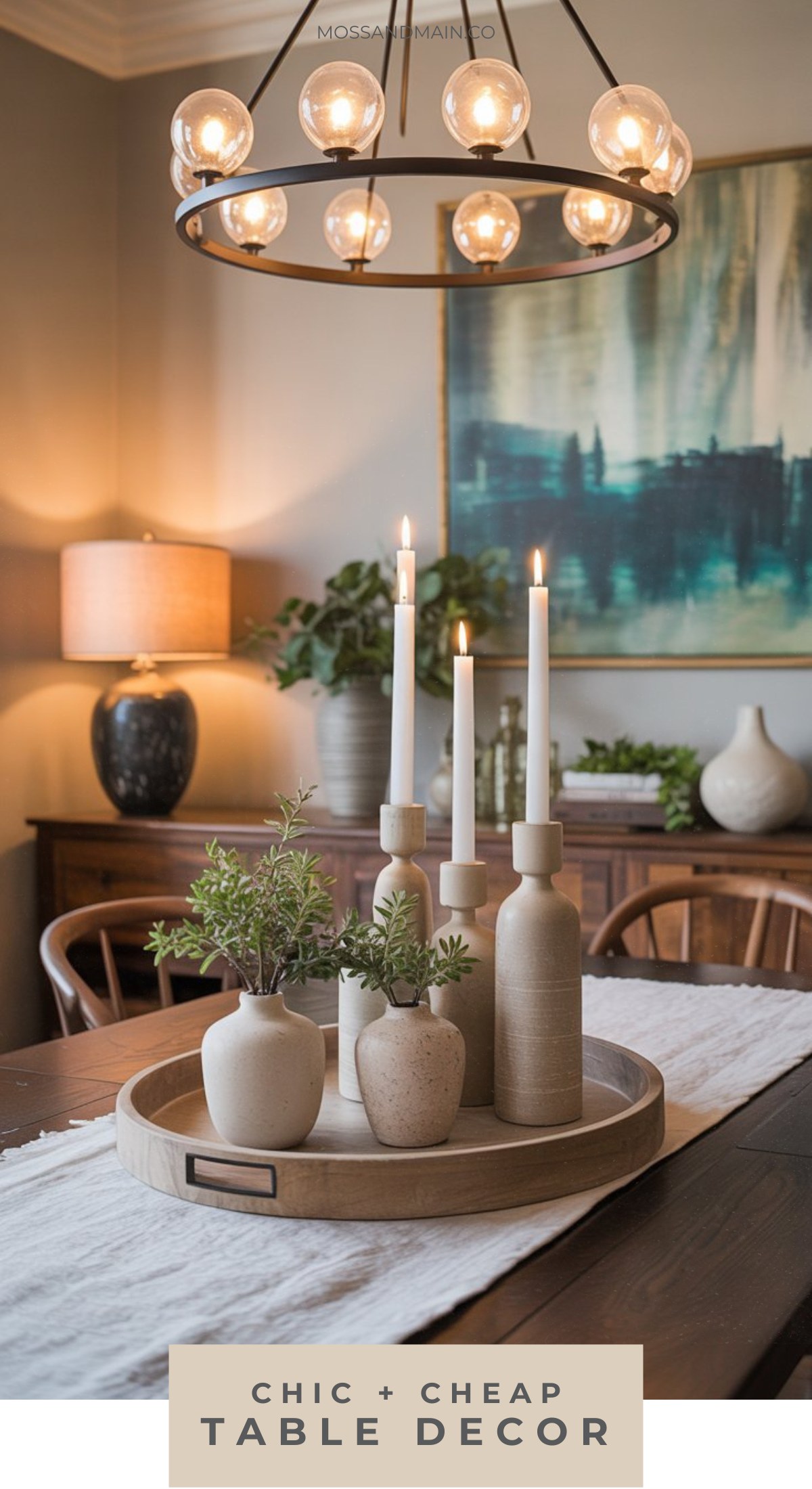 A dining table with a wooden tray holding vases, candles, and greenery showcases Organic Chic style. A modern chandelier hangs above, with plants and abstract art in the background. Text reads, Chic + Cheap Dining Room Table Decor.