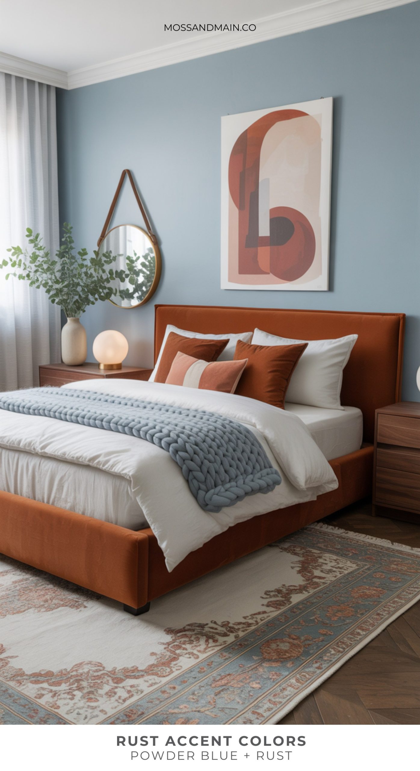 A modern bedroom with a rust-colored bed, rust and white pillows, a chunky blue knit blanket, and powder blue walls. Rust accent colors and wood furniture complete the cozy look, along with a round mirror and abstract wall art.