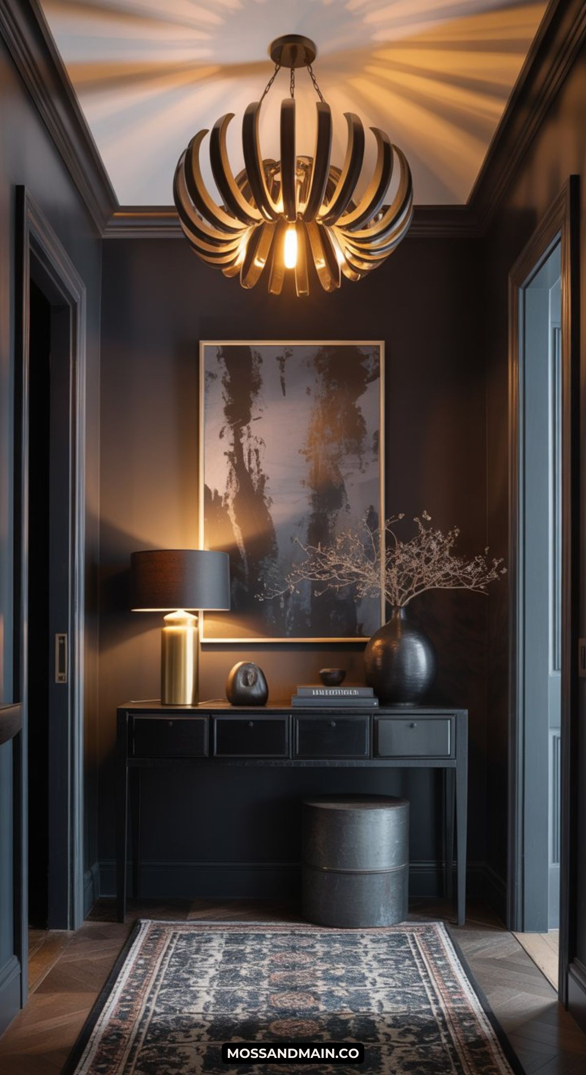 A dark and moody entryway features modern walls, a large abstract painting, a black console table with a lamp and decor, a patterned rug, and a unique sculptural chandelier casting warm light.