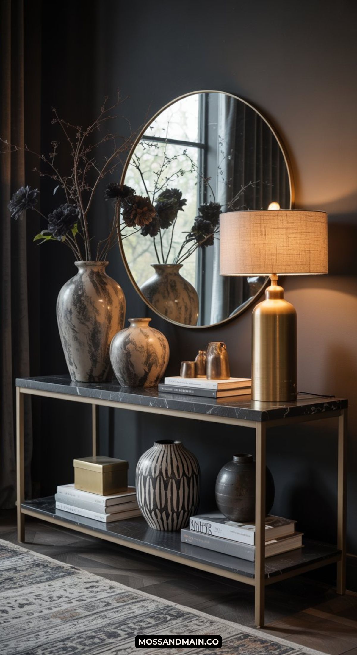 A modern console table with decorative vases, stacked books, a gold lamp, and a round mirror on a dark wall creates a stylish, sophisticated dark and moody entryway.