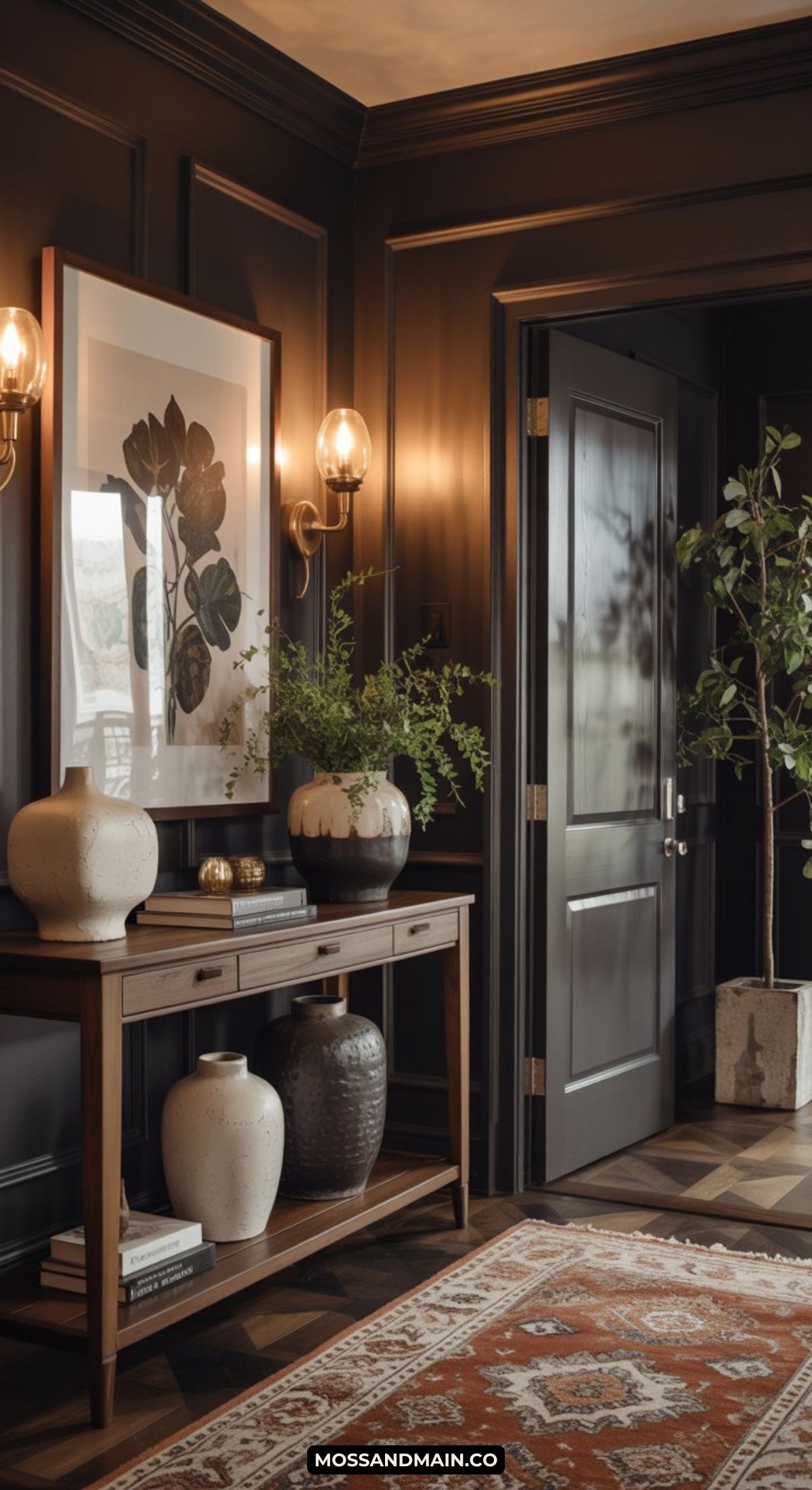 A dark and moody entryway features paneled walls, a wooden console table with decorative vases and greenery, a large framed floral artwork, wall sconces, an open door, and a patterned rug on a herringbone floor.