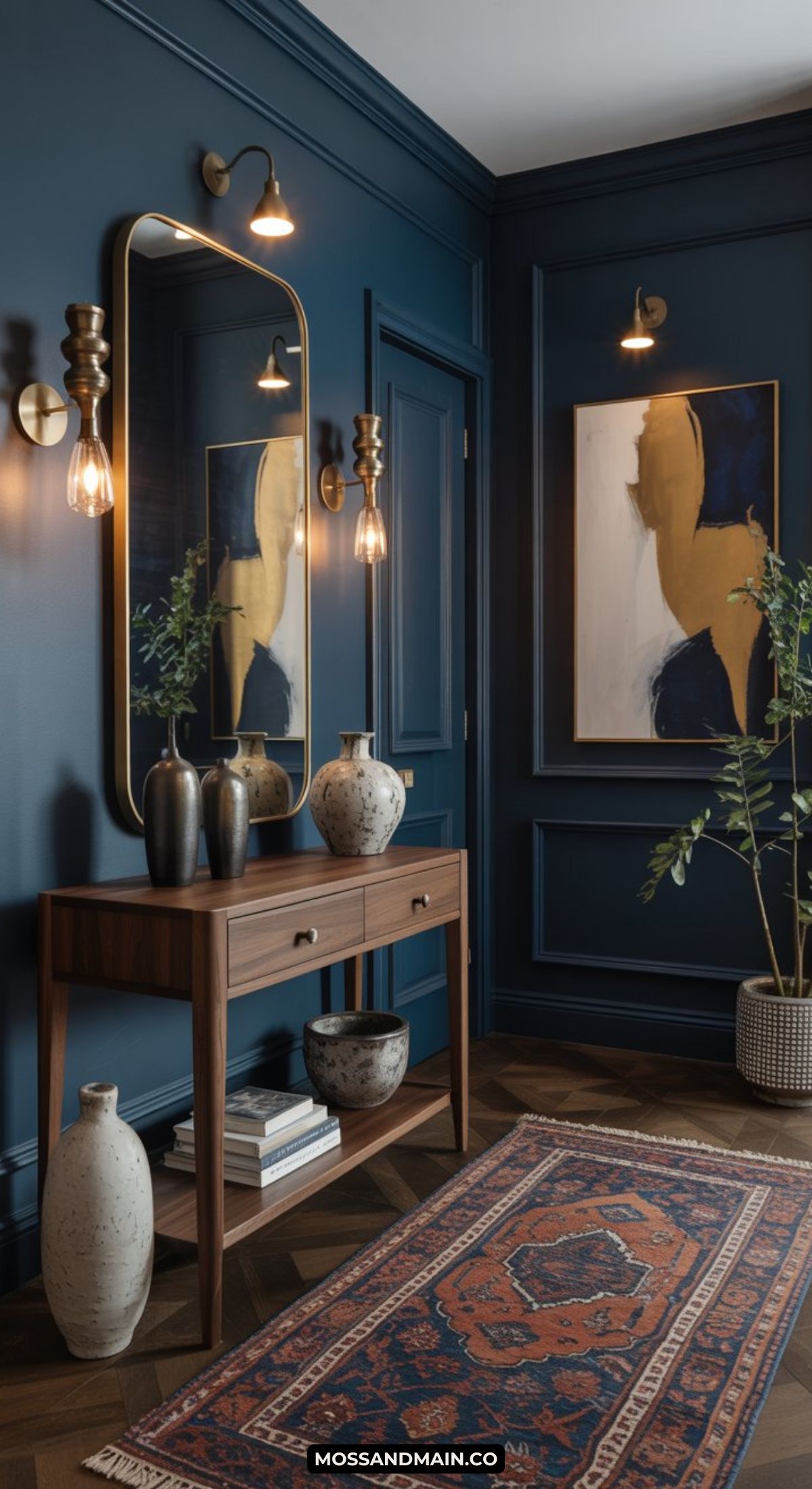 A modern, dark and moody entryway with deep blue walls, a wooden console topped with vases and plants, a large mirror, wall sconces, abstract art, and a patterned rug on herringbone wood flooring.