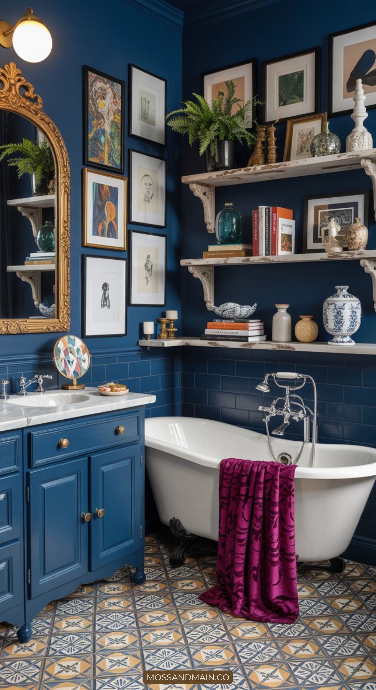 Eclectic blue bathroom with bold colors—vintage bathtub, blue vanity, patterned tile floor, gallery wall of art, gold-framed mirror, and shelves with books and decor. A magenta towel adds a maximalist color pop draped over the tub.