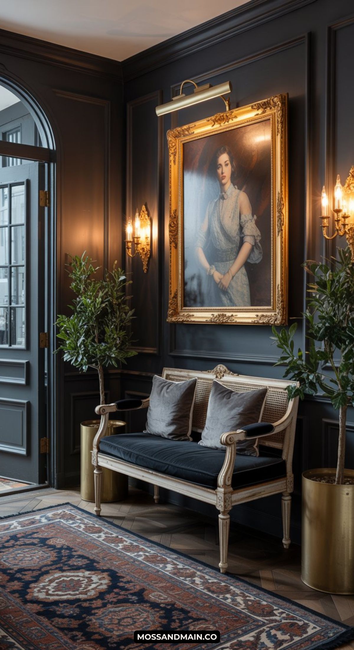 A stylish, dark and moody entryway features paneled walls, a classic wooden bench with cushions, two potted plants, and a large framed portrait. Warm lighting and a patterned rug create an elegant, inviting atmosphere.