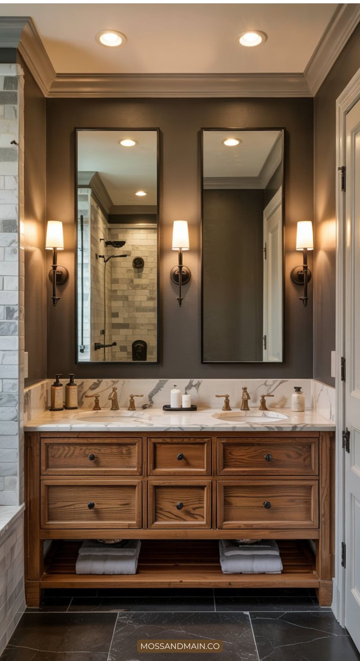 A modern bathroom showcasing 2026 bathroom trends features a wooden double-sink vanity, marble countertop, two rectangular mirrors, stylish wall sconces, and a walk-in shower with glass door. Towels are neatly stored on the shelf below the sinks.