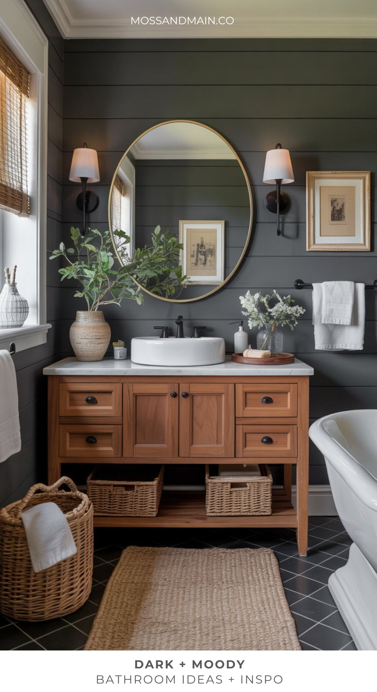 A stylish, moody bathroom features dark shiplap walls, a wooden vanity with a vessel sink, a round mirror, wicker baskets, wall sconces, framed art, and greenery for a modern yet timeless look.