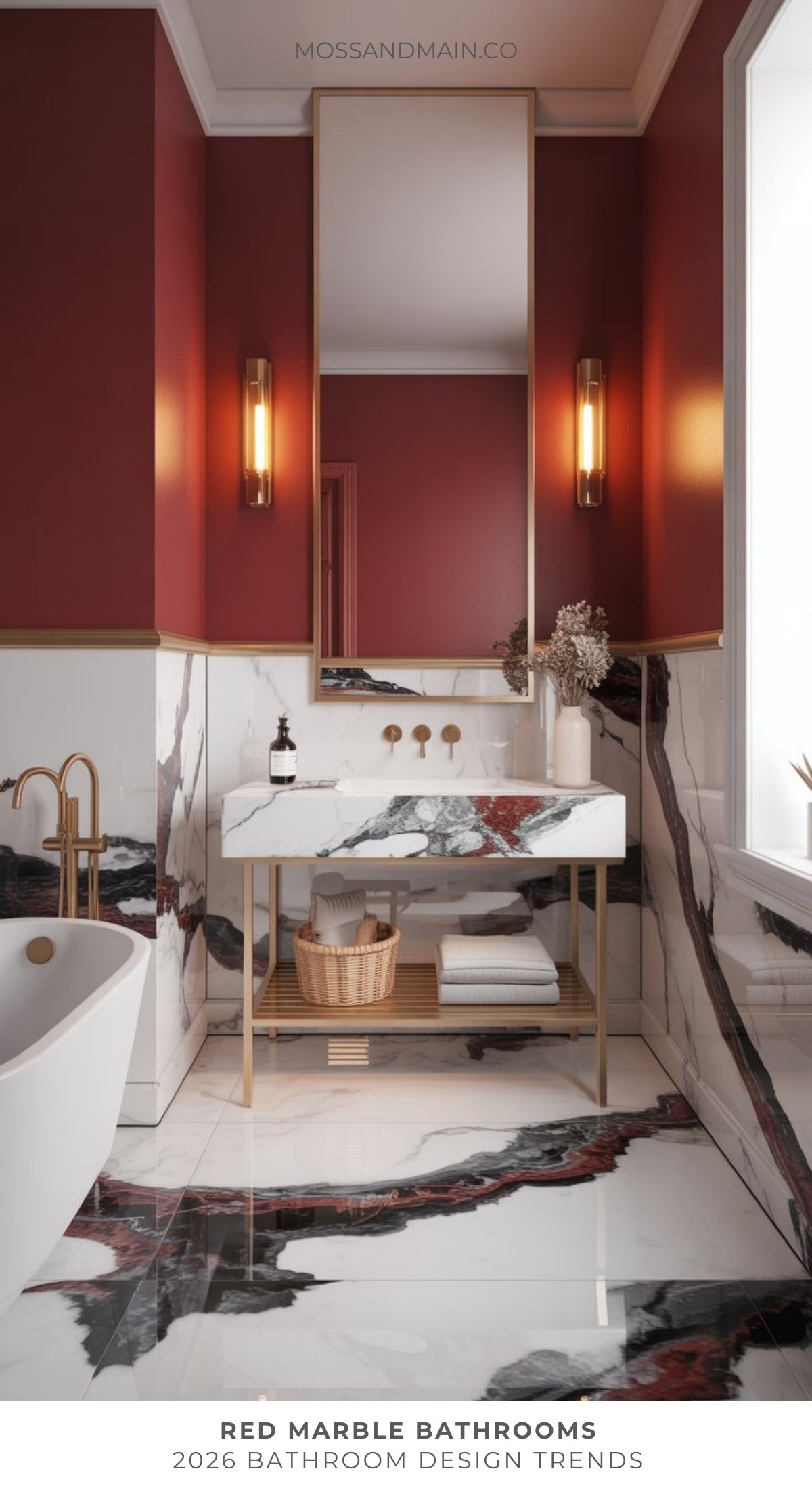 A modern bathroom trend features bold red walls, a tall mirror, gold fixtures, and a white vanity with striking red and black marble. Marble extends onto the floor and wall. A white tub and natural light complete this bold bathroom space.