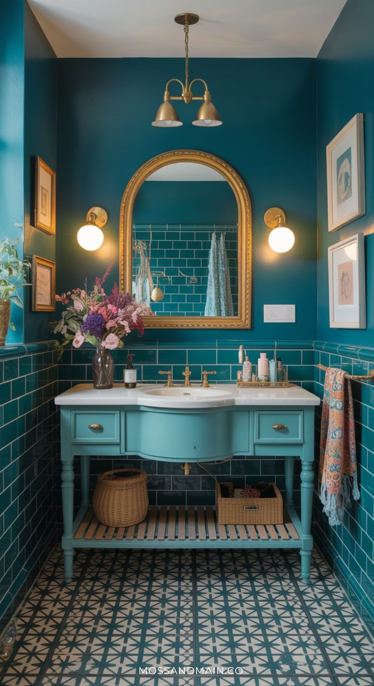 A stylish moody bathroom with teal walls and tiles, a vintage vanity, a gold-framed oval mirror, modern lighting, floral arrangement, and patterned floor tiles creates an elegant, cozy atmosphere with dramatic bathroom flair.