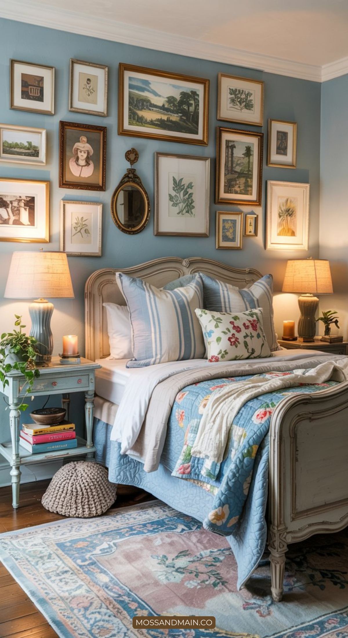 A cozy cottagecore bedroom with a vintage bed, blue quilt, patterned pillows, and blue walls. Two nightstands with lamps, plants, books, and a storybook cottagecore gallery wall create charm above the bed. A patterned rug warms the wooden floor.