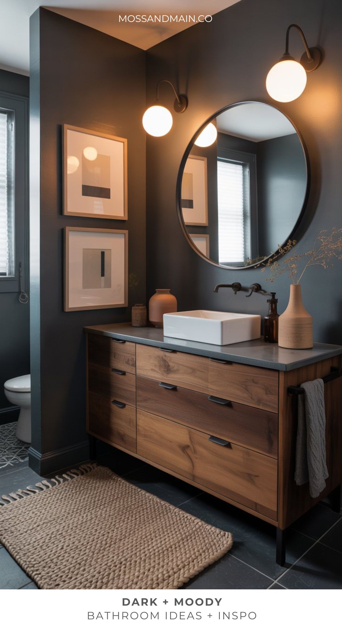 A modern, dramatic bathroom with dark walls, a round mirror, wooden vanity and white vessel sink. Minimalist decor, warm lighting, and framed art offer inspiring dark bathroom ideas for a stylish, moody atmosphere.