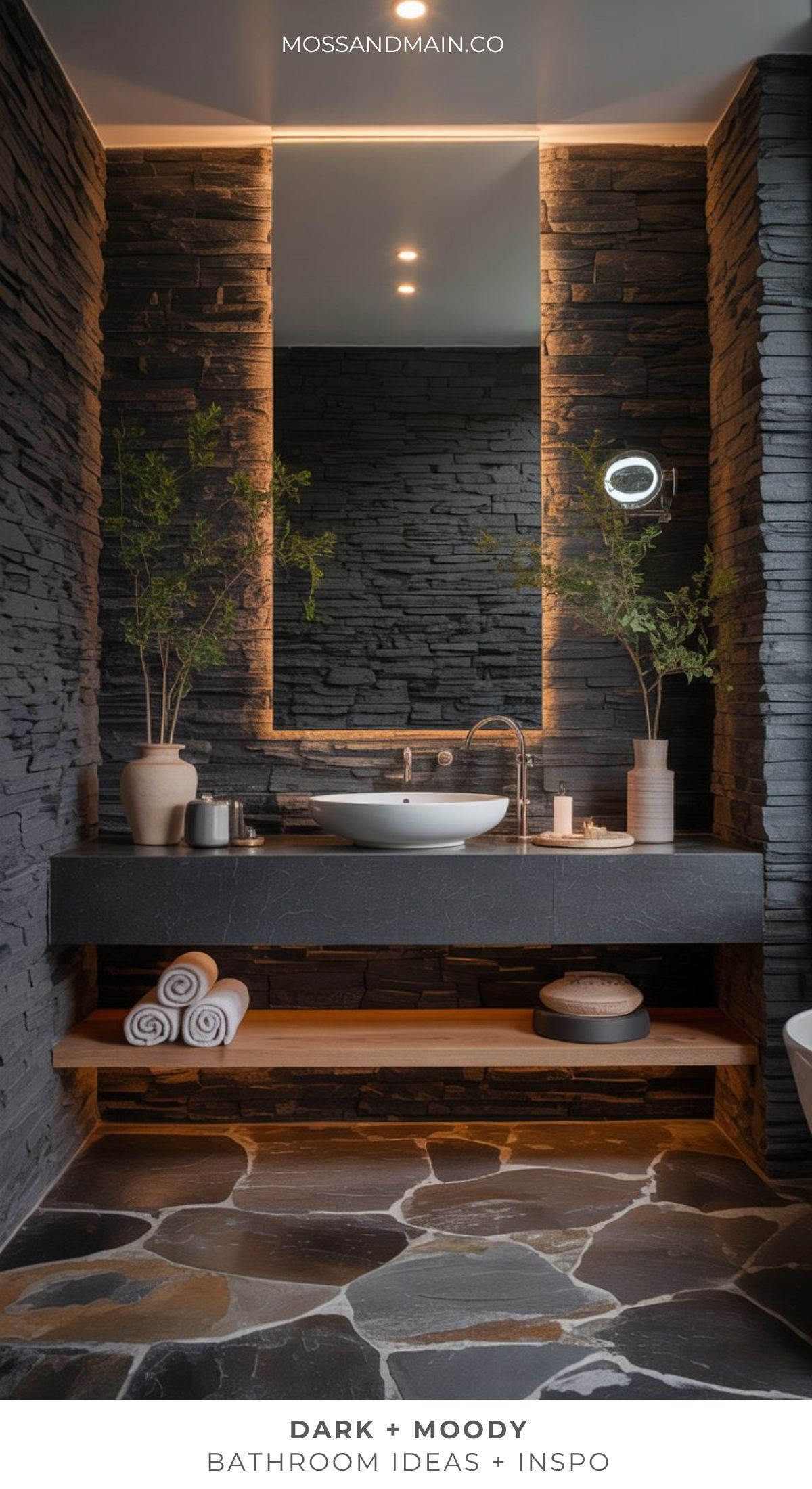 A modern bathroom with dark stone walls, a large mirror, a round sink on a black countertop, minimalist decor, rolled towels, and soft lighting—perfect for those seeking dramatic bathroom elegance and moody bathroom inspiration.