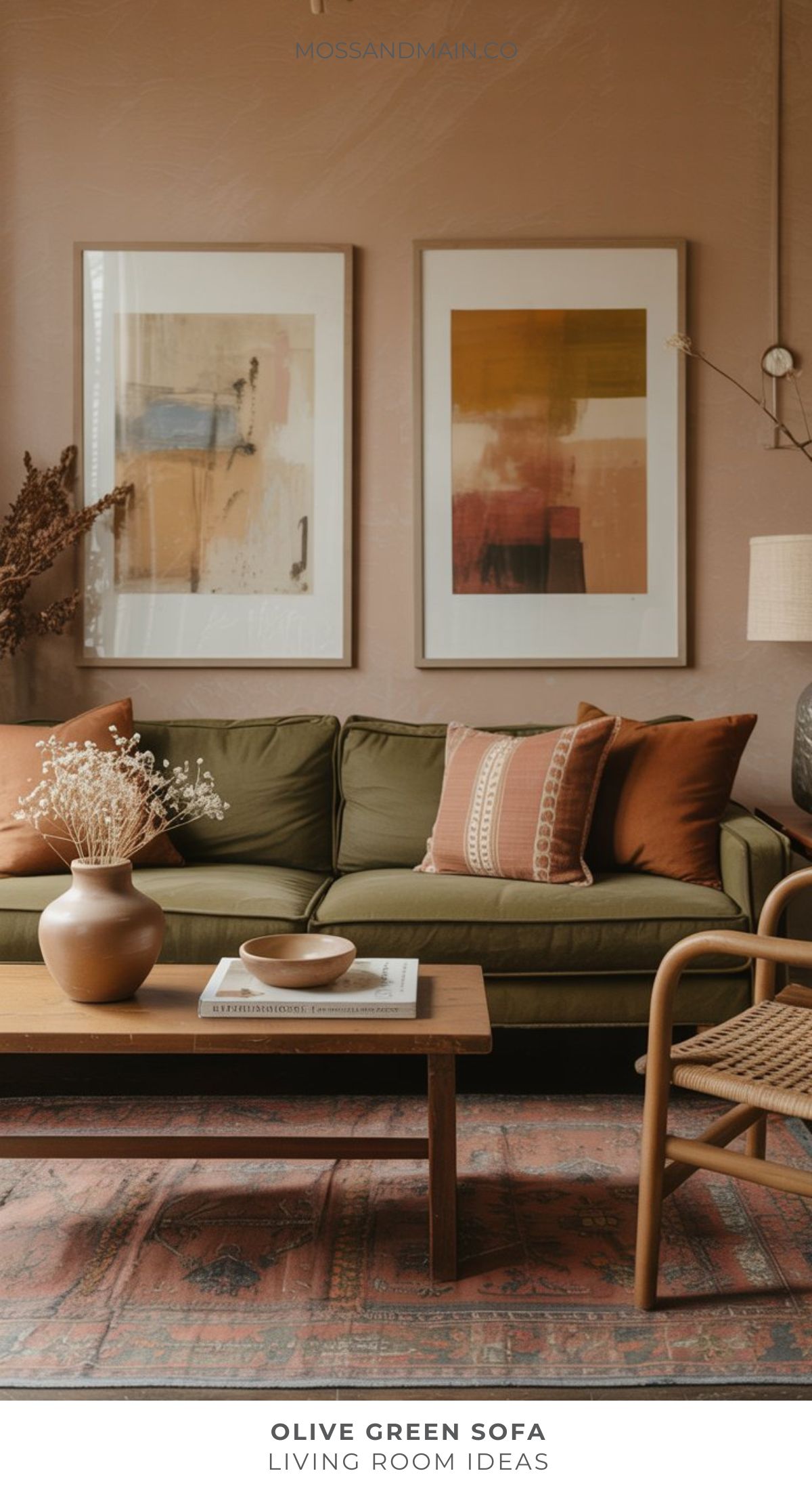 An olive green sofa with rust and beige pillows sits in a cozy living room with abstract art on the wall—a perfect source of inspiration for designers seeking fresh living room ideas. A wooden coffee table, dried flowers, woven chair, and patterned rug complete the look.