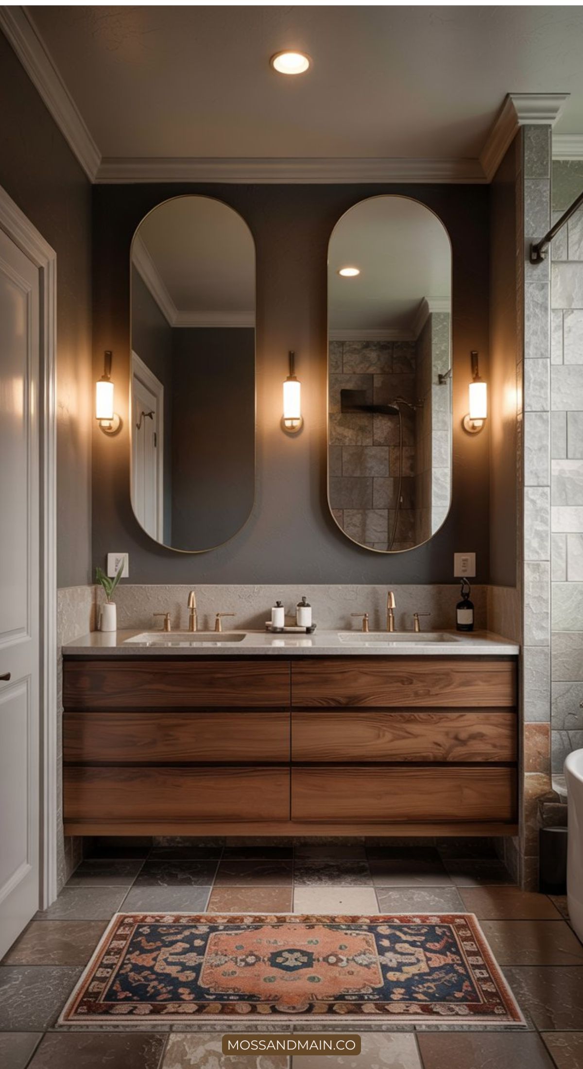 A modern bathroom design with a double sink vanity featuring wood drawers, two oval mirrors, wall sconces, gray walls, tiled floor, and a decorative rug. A glass shower and white bathtub complete this showcase of 2026 bathroom trends.
