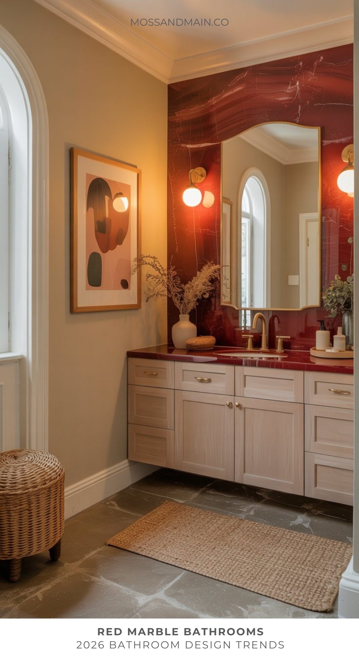 A bold bathroom with a red marble backsplash, gold fixtures, light wood vanity, round mirror, wall art, a wicker basket, and neutral walls—styled with modern decor and soft lighting for the latest bathroom trend.