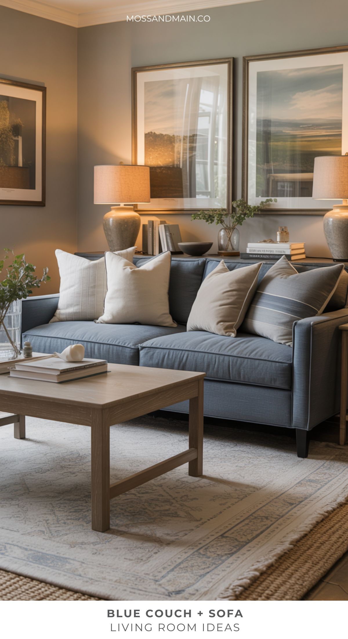 A blue couch living room features beige and gray pillows, a light wood coffee table, table lamps, and framed landscape art on taupe walls. A neutral patterned rug covers the floor for a cozy touch.