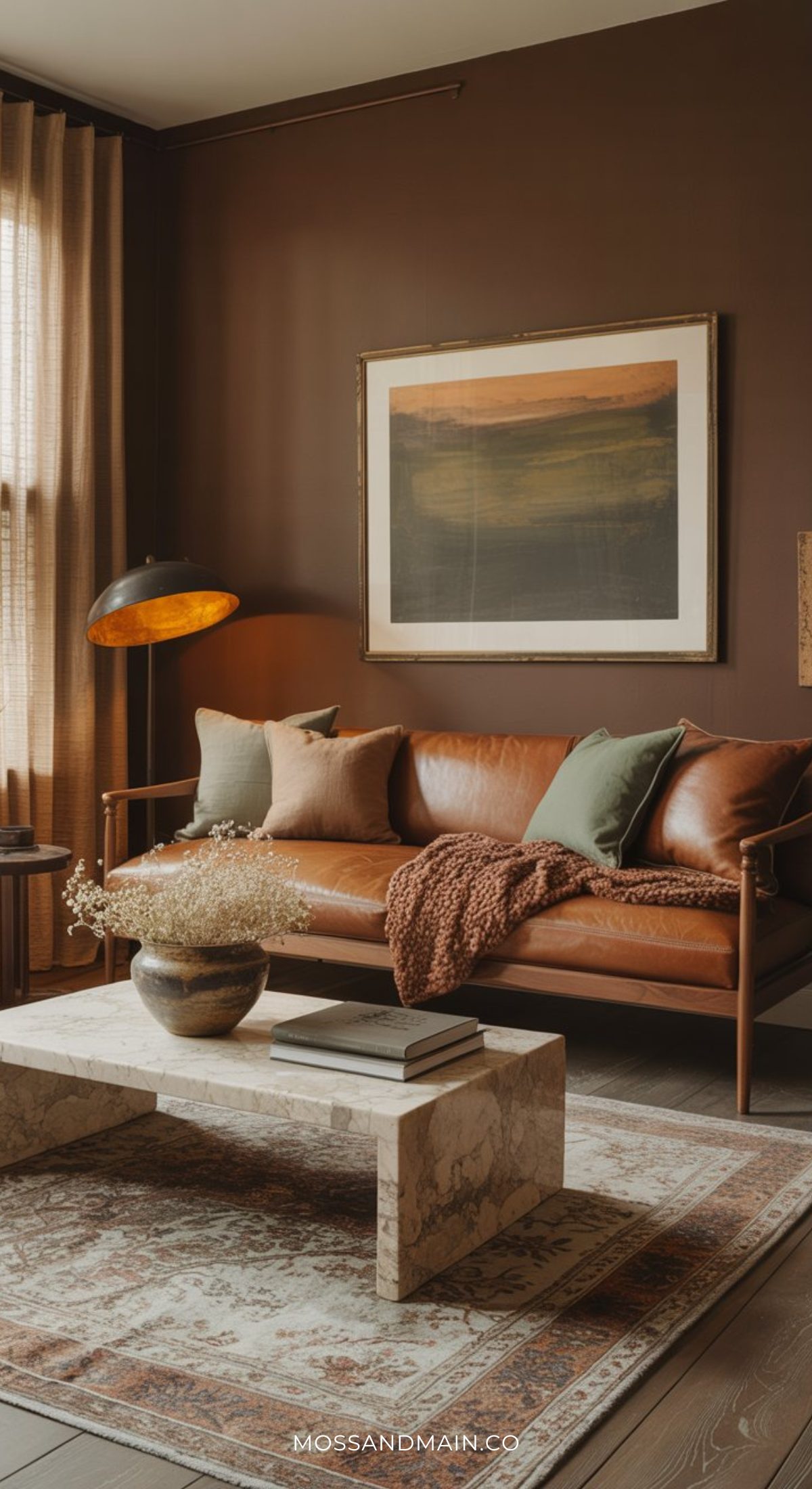 A cozy living room inspired by the psychology of color features a brown leather sofa with green and brown pillows, a textured blanket, marble coffee table, patterned rug, earth-toned walls, large art, and soft natural light—perfect for a soulful home in 2026.