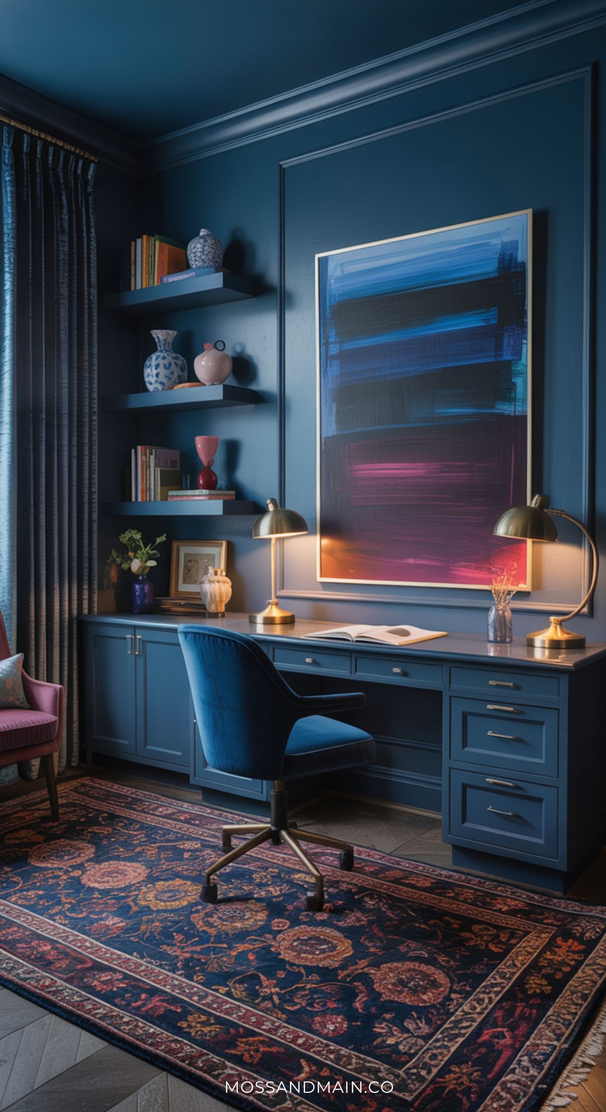 A stylish home office highlights Home Office Design trends with a navy blue desk, matching chair, lamp, decorative shelves, vibrant abstract art, and a patterned rug set against deep blue walls and a large curtained window.