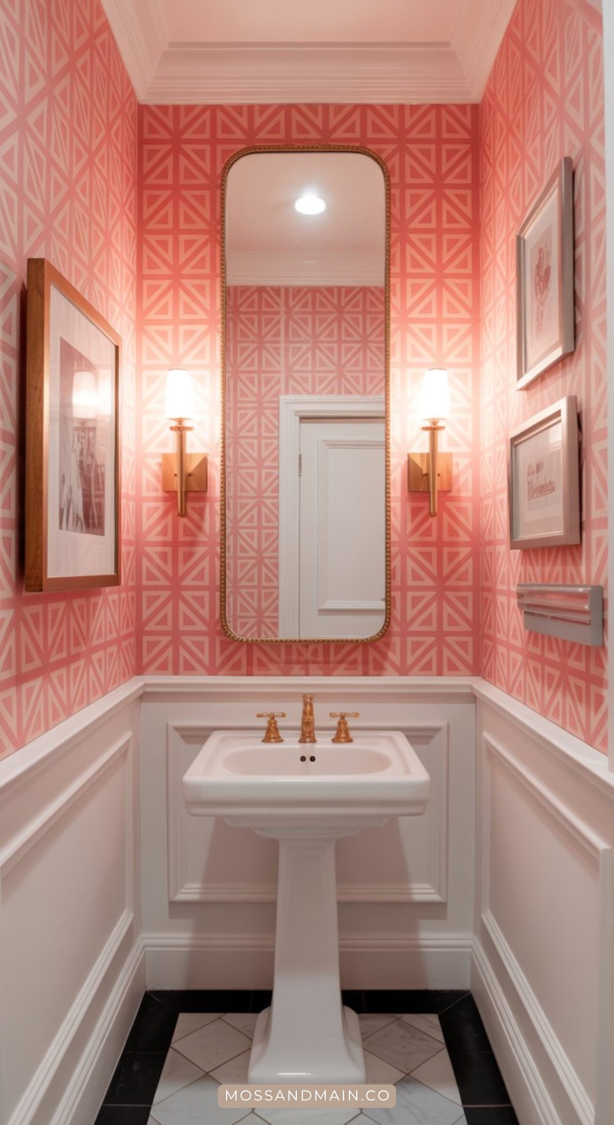 A stylish bathroom featuring pink geometric wallpaper, a tall mirror above a white pedestal sink, brass fixtures, white wainscoting, framed art, and black-and-white tile floor—perfect inspiration for pink bathroom ideas.