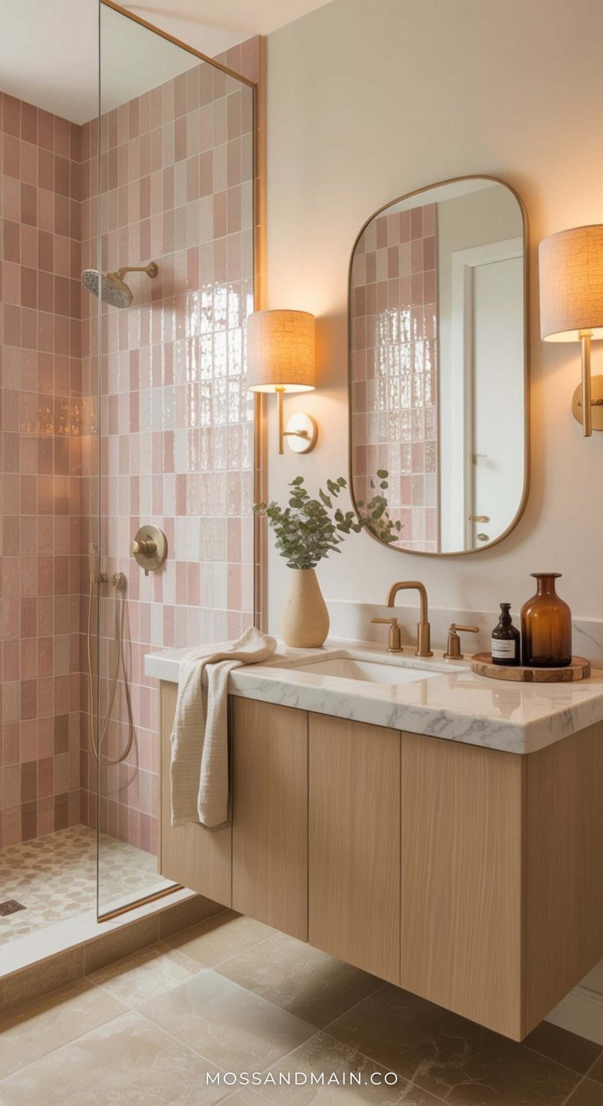 Modern and stylish bathroom with a wood vanity, marble countertop, oval mirror, and wall sconce. The shower features bold pink tiles and gold fixtures, separated by a glass partition for chic pink bathroom ideas.