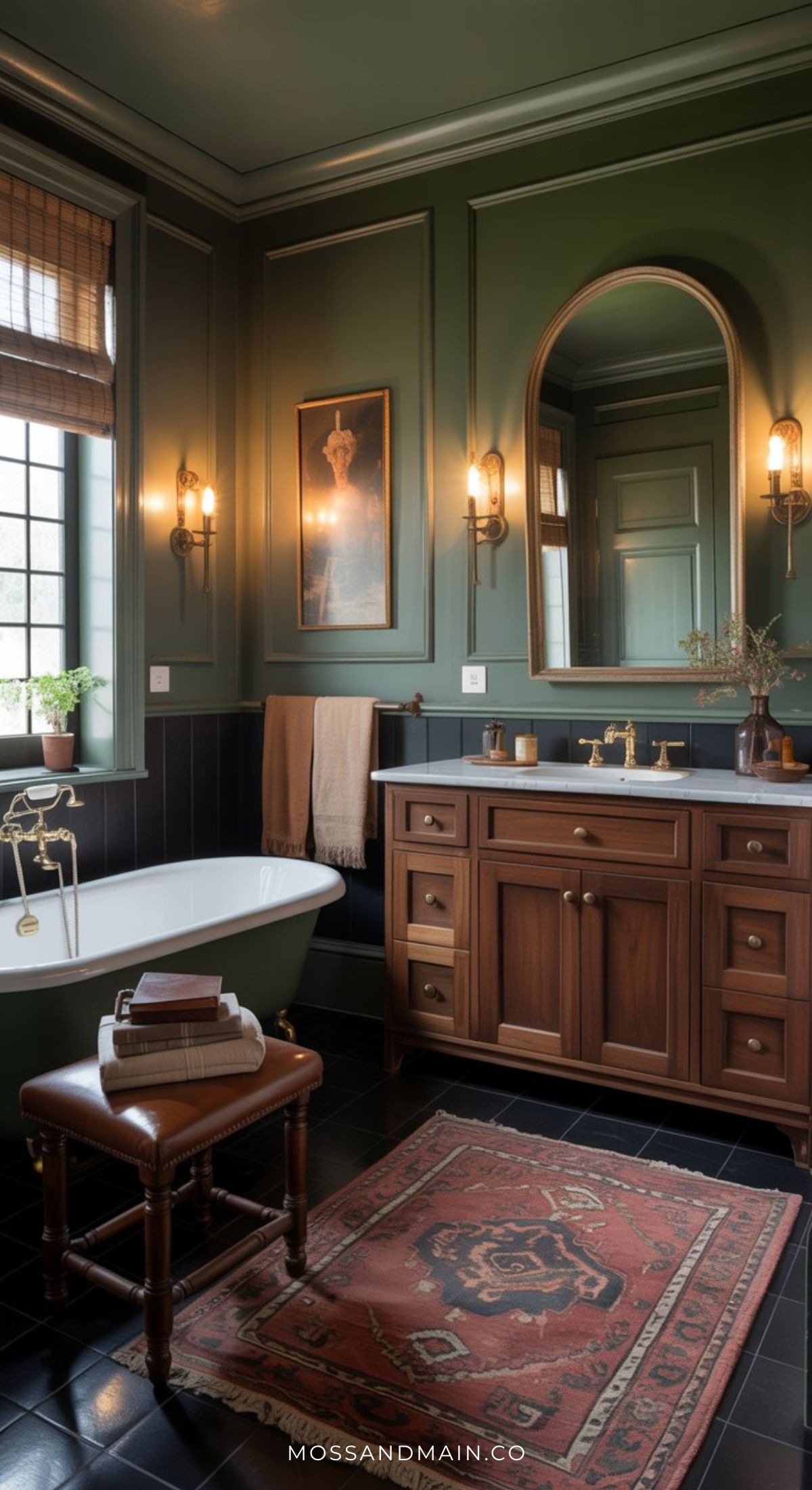 An elegant sage green bathroom with dark walls, a vintage rug, clawfoot bathtub, wooden vanity with brass fixtures, framed mirror, and wall sconces. Natural light filters in through a window with bamboo shades for a cozy touch.