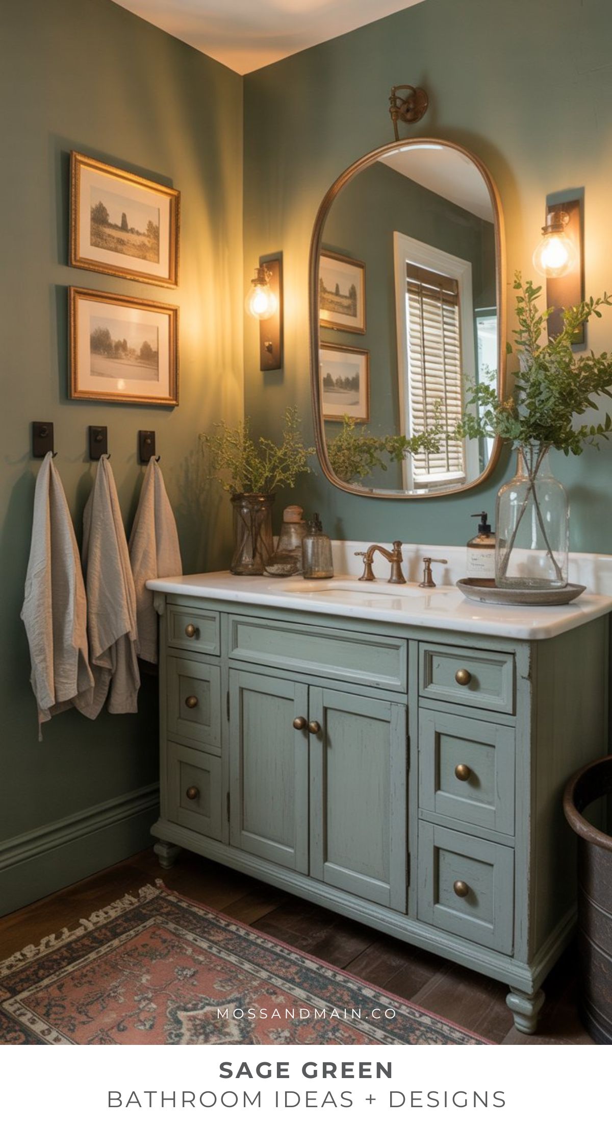 A cozy bathroom with sage green walls, a matching vanity, bronze fixtures, a large oval mirror, wall art, vases with greenery, towels on hooks, and soft lighting creates an elegant and inviting sage green bathroom atmosphere.