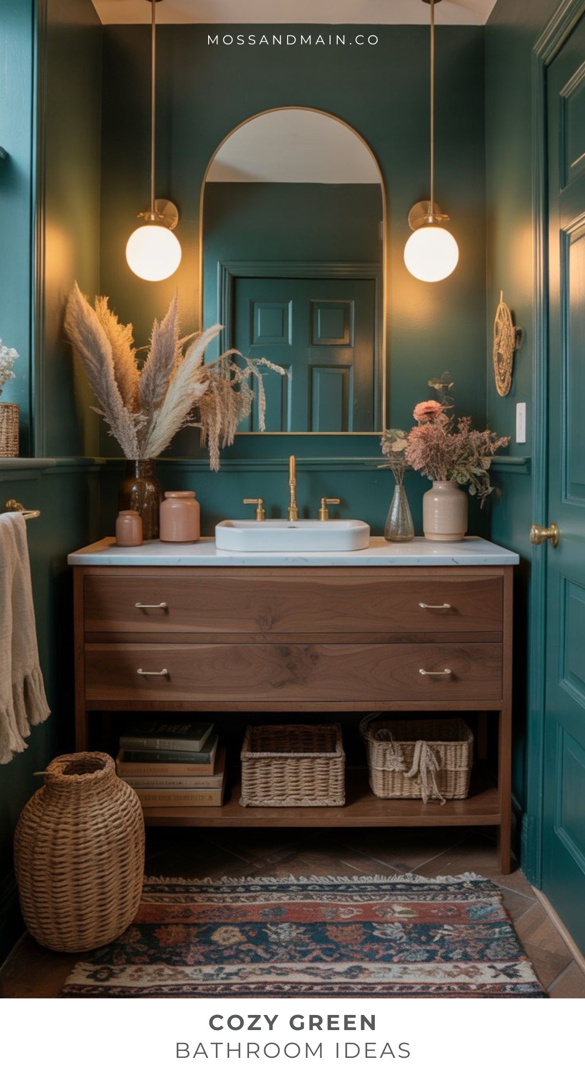 A stylish sage green bathroom with deep green walls, a wooden vanity and white sink, round mirror, globe lights, woven baskets, dried flowers in vases, and a patterned rug creates a cozy and inviting atmosphere—perfect for bathroom ideas.