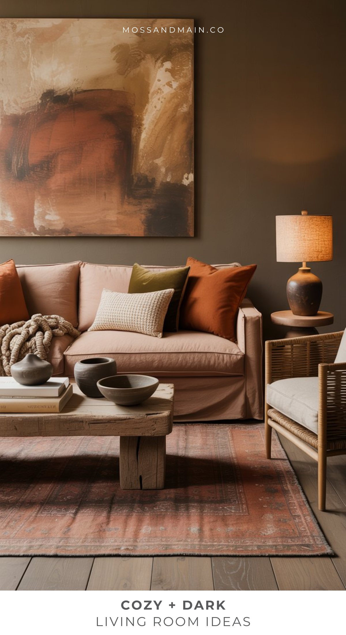 A cozy living room with a blush sofa, rust and cream pillows, wooden coffee table, woven chair, warm table lamp, abstract wall art, and earthy tones—perfect dark living room ideas for creating a moody living room retreat. COZY + DARK LIVING ROOM IDEAS.