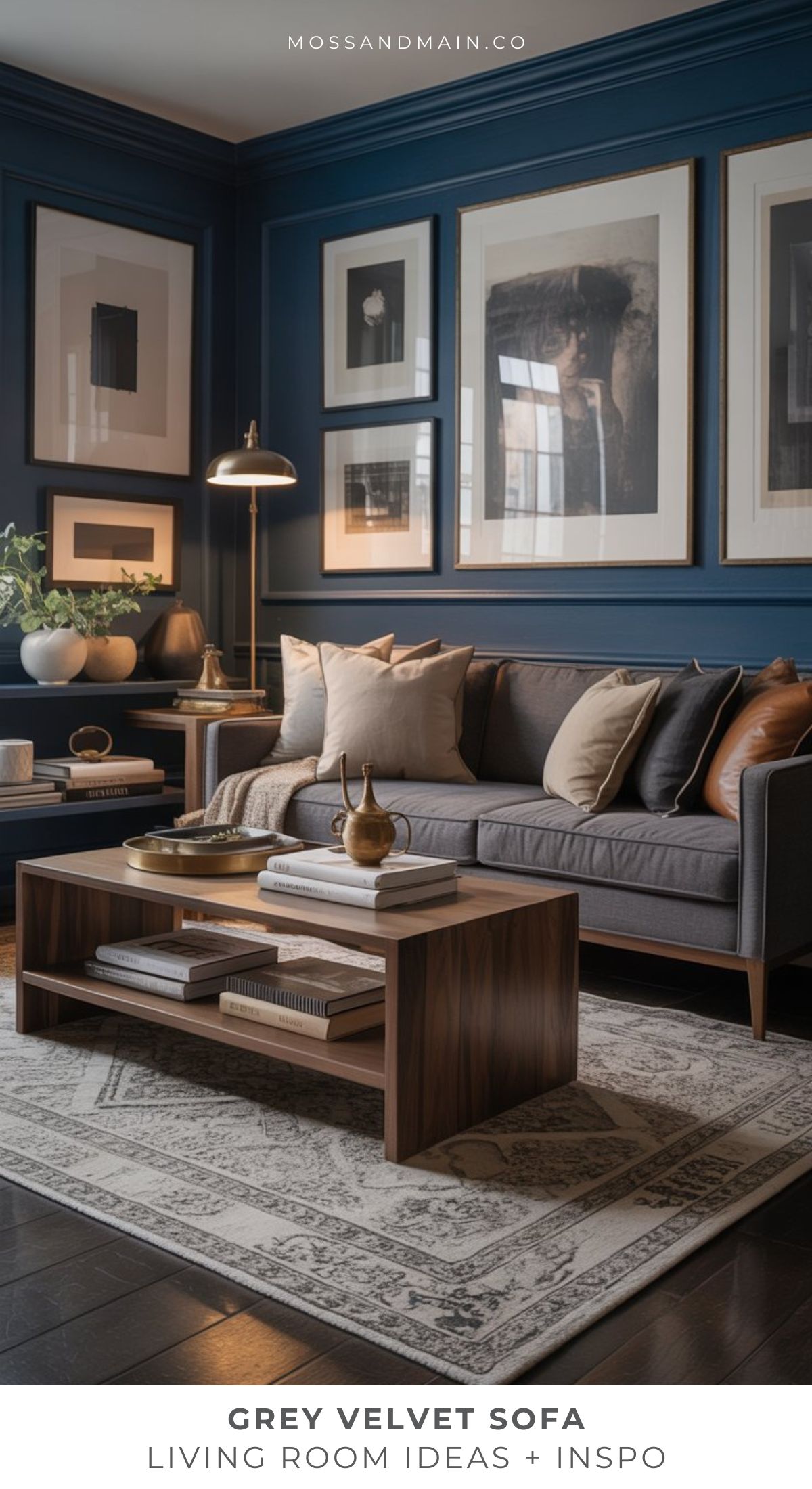 A stylish grey sofa living room with a velvet sofa, wooden coffee table, decorative pillows, framed wall art, a rug, and houseplants—all set against dark blue walls and warm lighting.