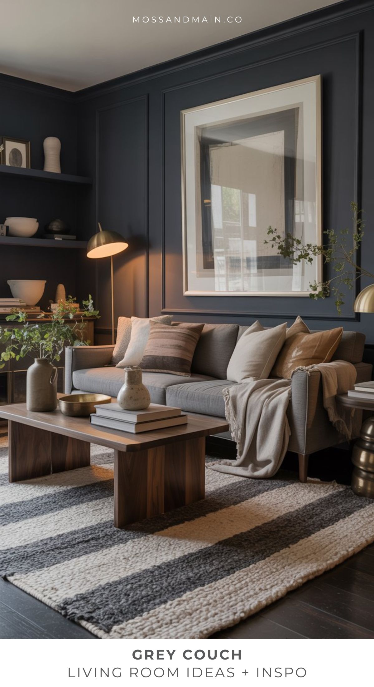 A modern grey sofa living room with a striped rug, wooden coffee table, minimalist decor, plants, and dark walls showcasing large framed art. Warm lighting enhances the cozy atmosphere.