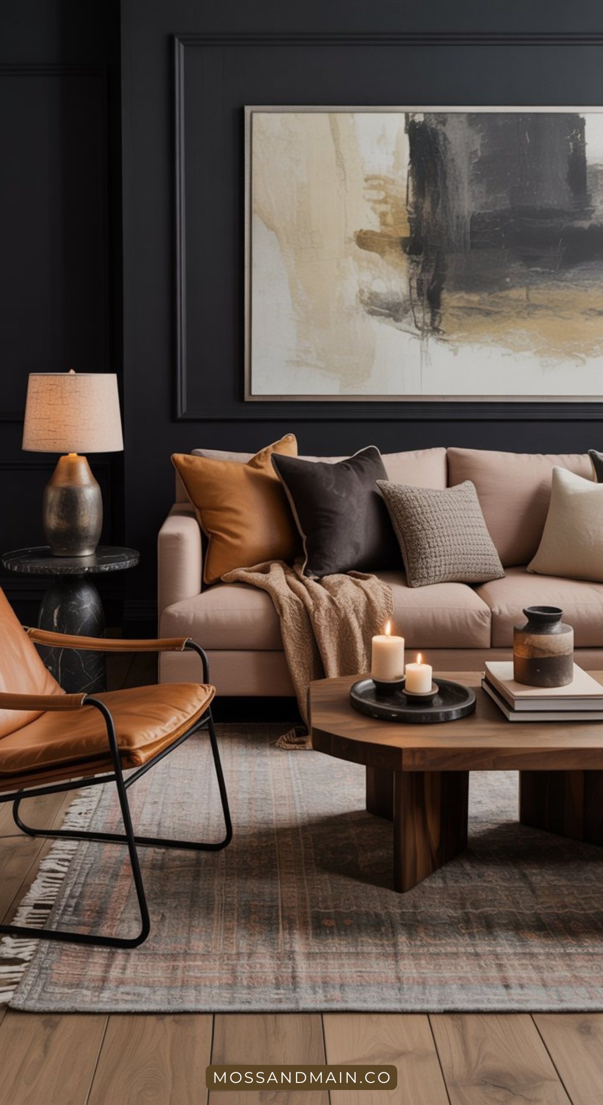 A modern, cozy living room with a beige sofa, brown and gray cushions, a leather accent chair, and a round wooden coffee table. Moody living room touches like candles, books, and abstract art on a dark wall complete the inviting space.