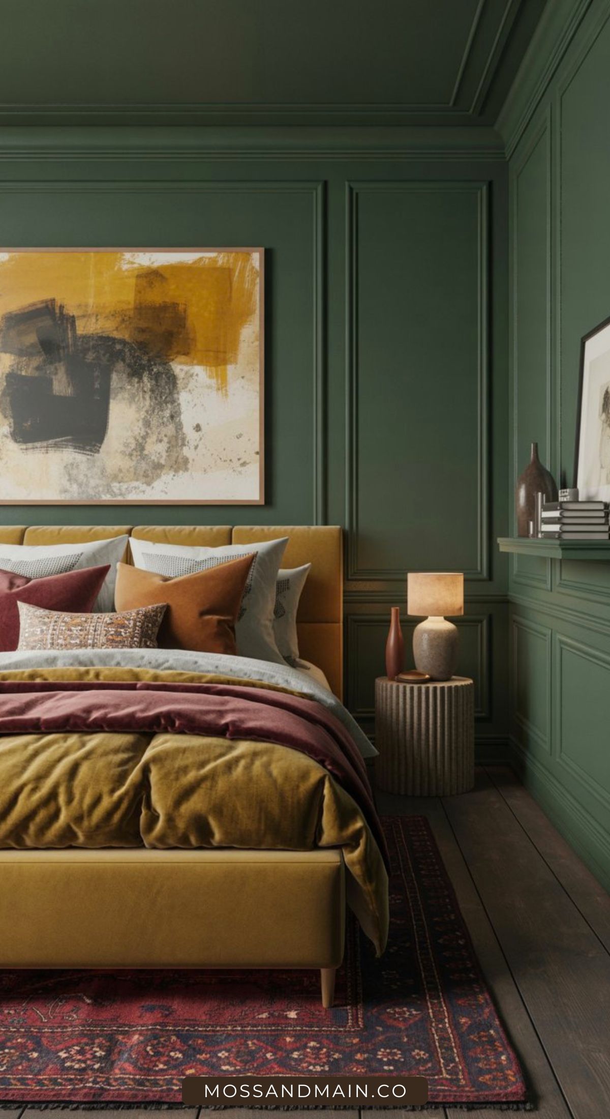 A stylish bedroom with green paneled walls, a mustard yellow bed with layered pillows and blankets, a modern abstract painting, a side table with a lamp, vases, and books, and a patterned rug on a wooden floor.