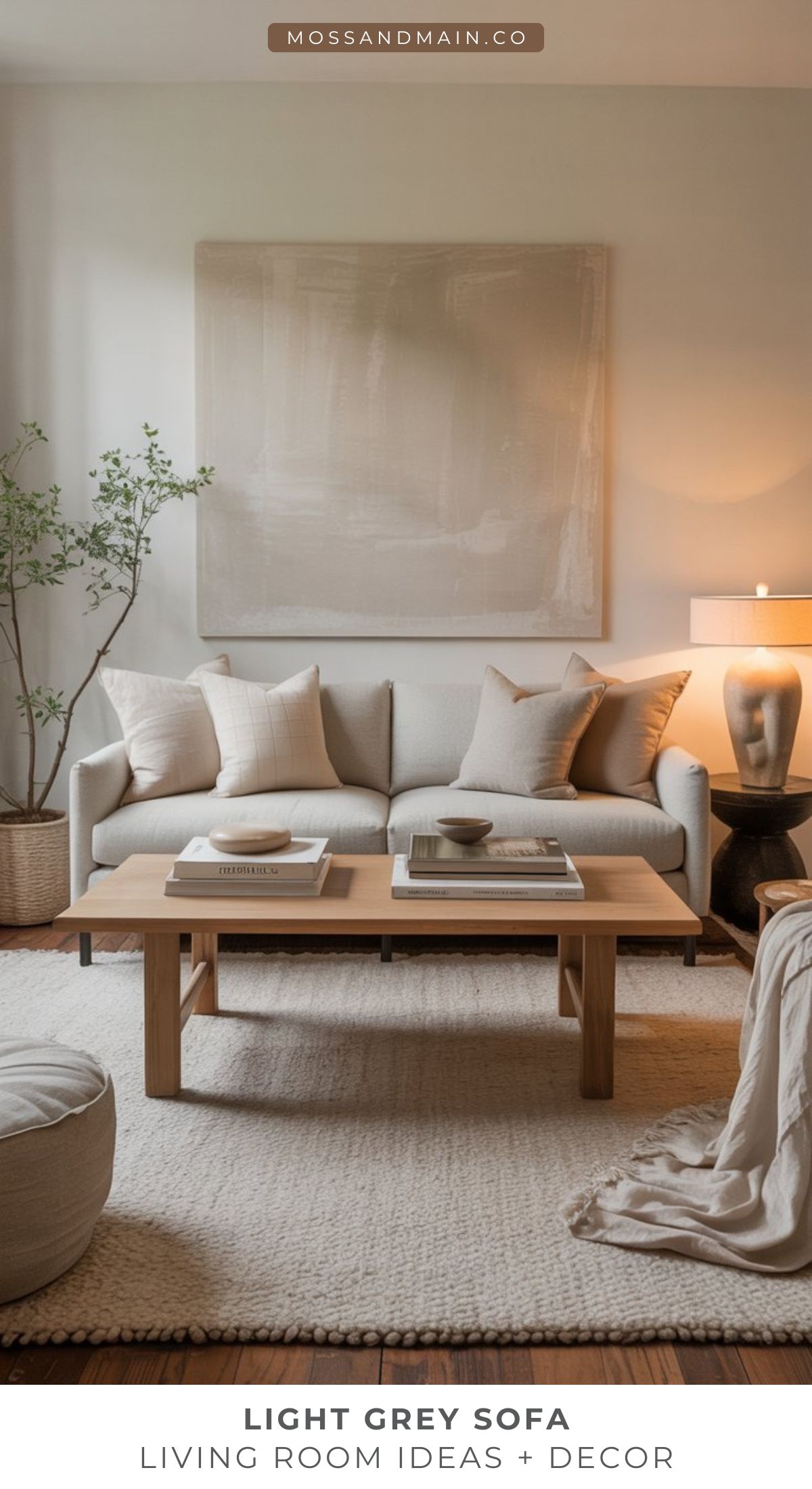 A modern living room with a light gray couch, neutral pillows, a wooden coffee table with books, a textured rug, large abstract wall art, a potted plant, and a warm table lamp—perfect for cozy living room ideas.
