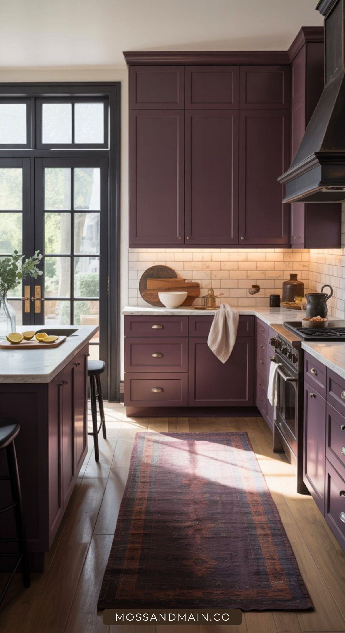 A modern kitchen with deep plum cabinets, white subway tile backsplash, a wooden countertop, island seating, and a patterned rug. Natural light streams through large glass doors on the left—perfect for those seeking bold aubergine kitchen ideas.