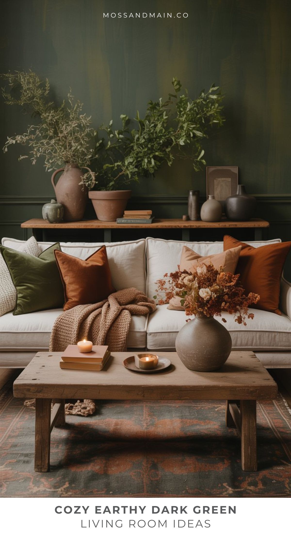 A cozy living room featuring a dark green wall, a beige sofa with rust and green pillows, earthy vases with dried flowers, wooden coffee table, candles, and a brown knit blanket. Perfect inspiration for earthy living room ideas.