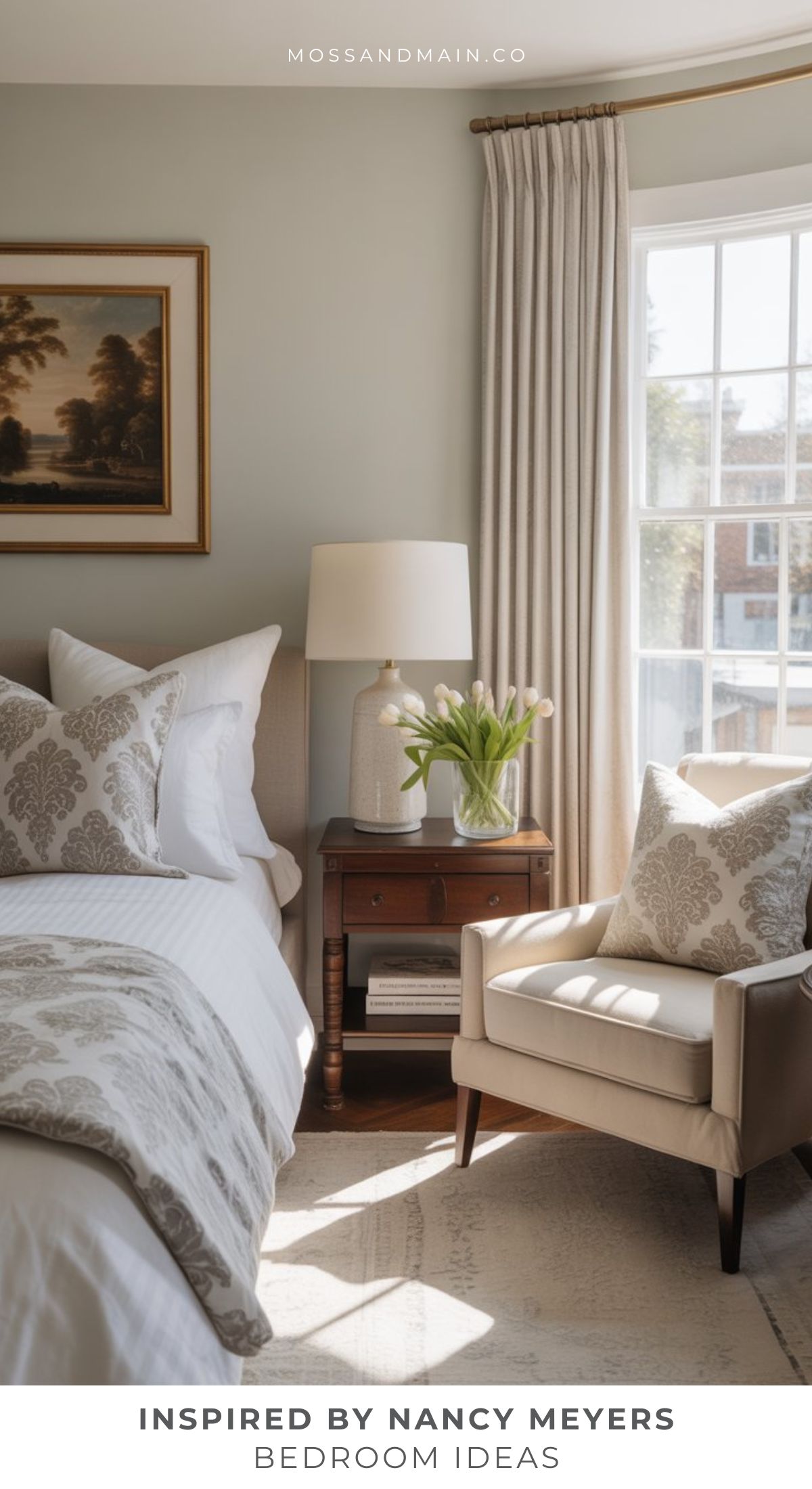A cozy, sunlit bedroom with a beige armchair, wooden nightstand, and tulips evokes a true Nancy Meyers aesthetic. Patterned bedding and framed art complete this inviting Nancy Meyers bedroom, where light curtains frame a large window.