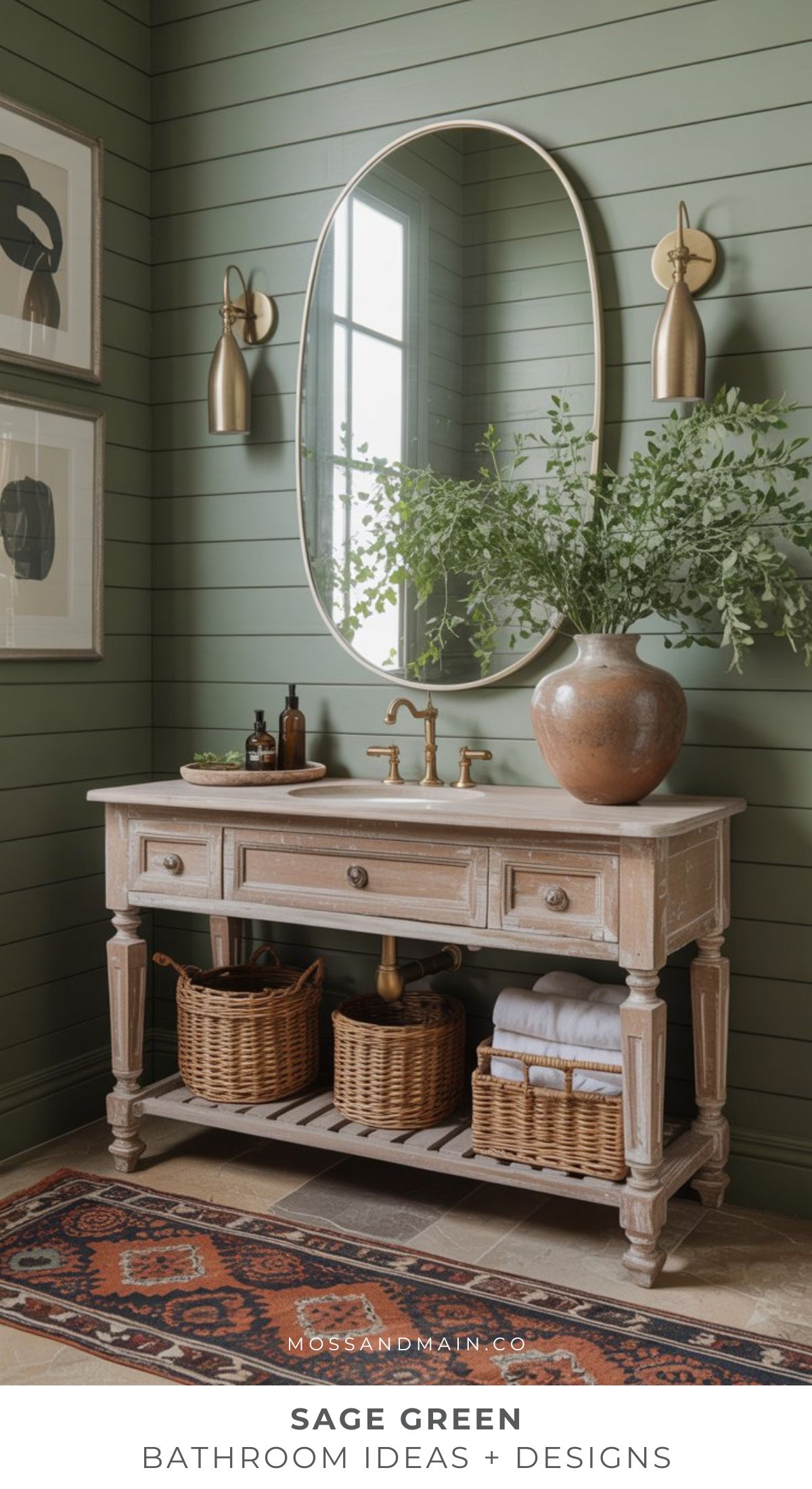 A cozy bathroom featuring sage green shiplap walls, a wooden vanity with gold fixtures, an oval mirror, wall sconces, baskets, lush greenery in a vase, and a patterned rug. Text reads: “Sage Green Bathroom Ideas + Designs.”.