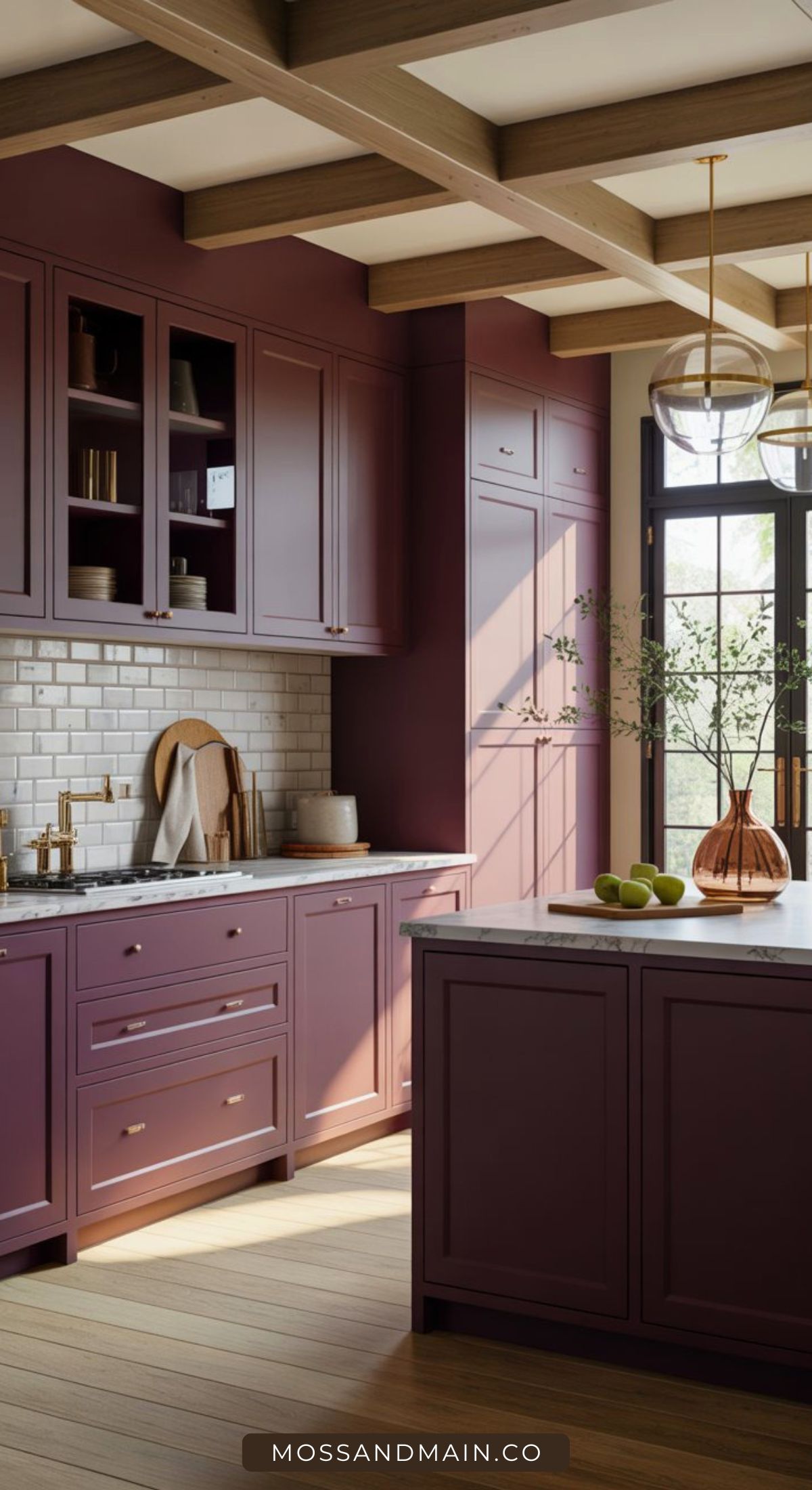 A modern kitchen with plum-hued cabinets, white subway tile backsplash, marble countertops, and wooden beams on the ceiling. A large window lets in natural light, illuminating a glass vase with branches and green apples on the island.