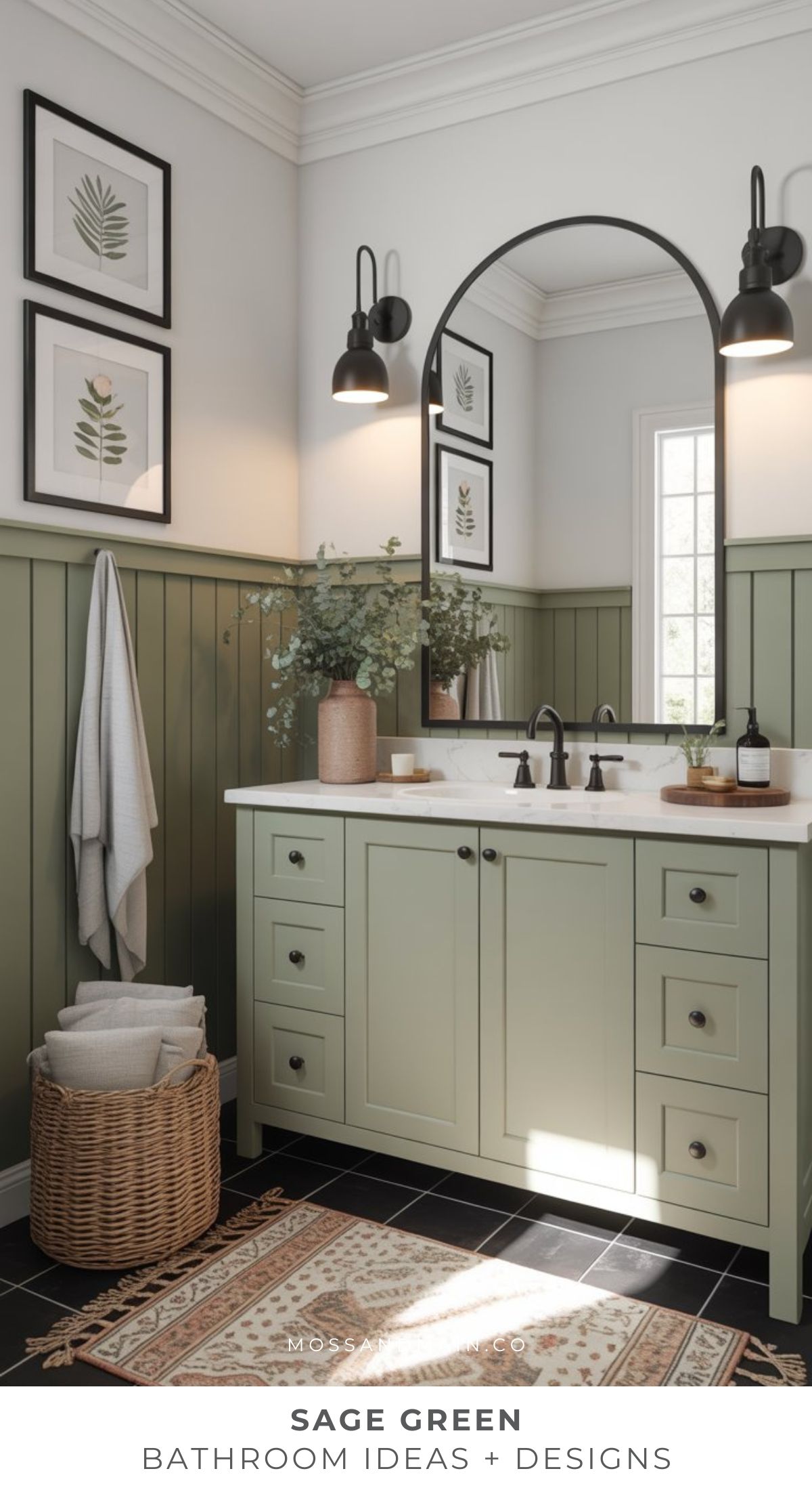 A cozy bathroom with sage green wainscoting and vanity, black fixtures, a round mirror, botanical wall art, a woven basket with towels, and a window filling the timeless bathroom with natural light.
