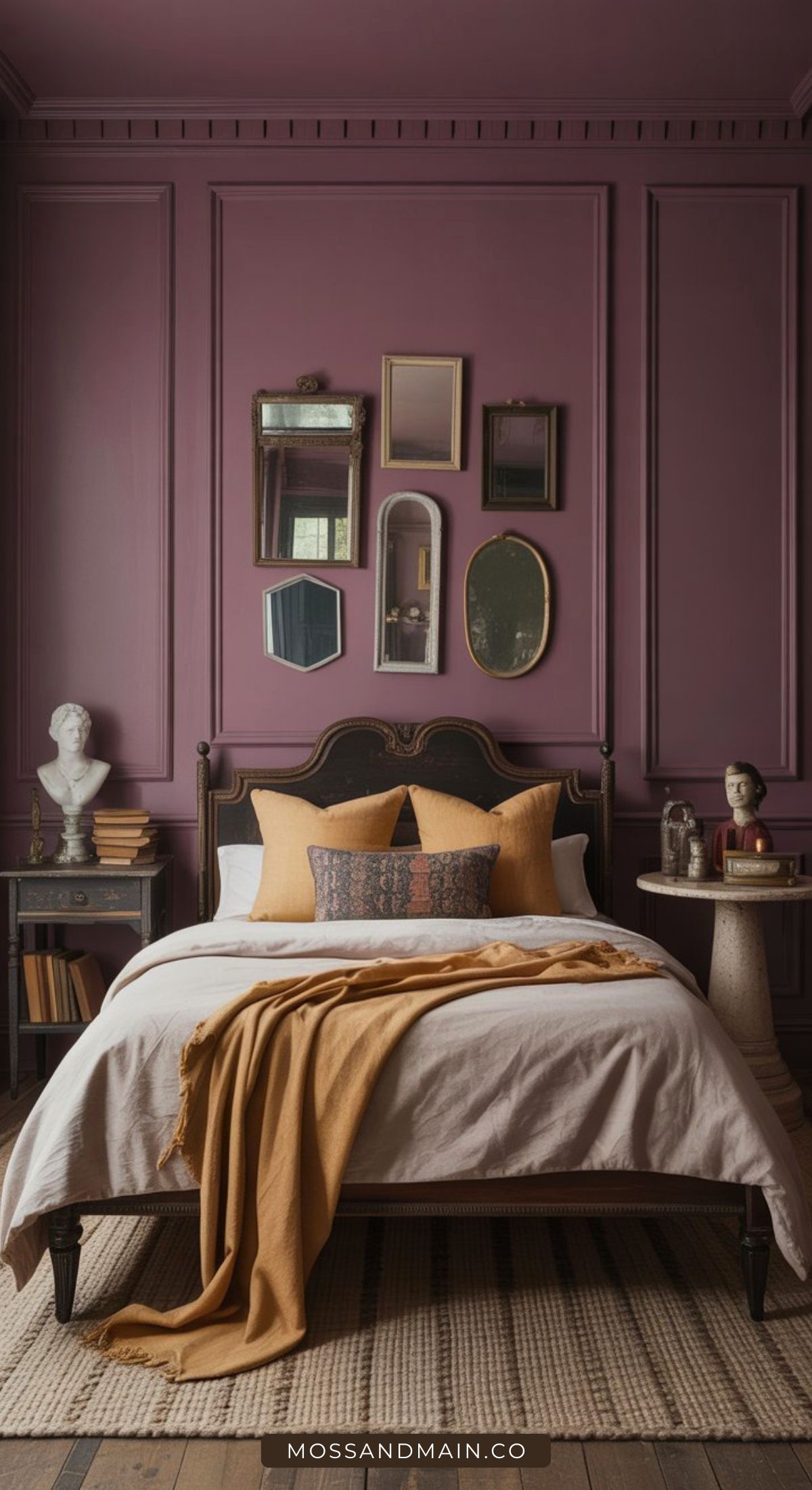 A cozy, color-drenched bedroom with mauve walls, a dark vintage bed frame, mustard bedding, and decorative pillows. Mirrors and art hang above the bed while sculptures and books on side tables create an elegant, maximalist bedrooms vibe.