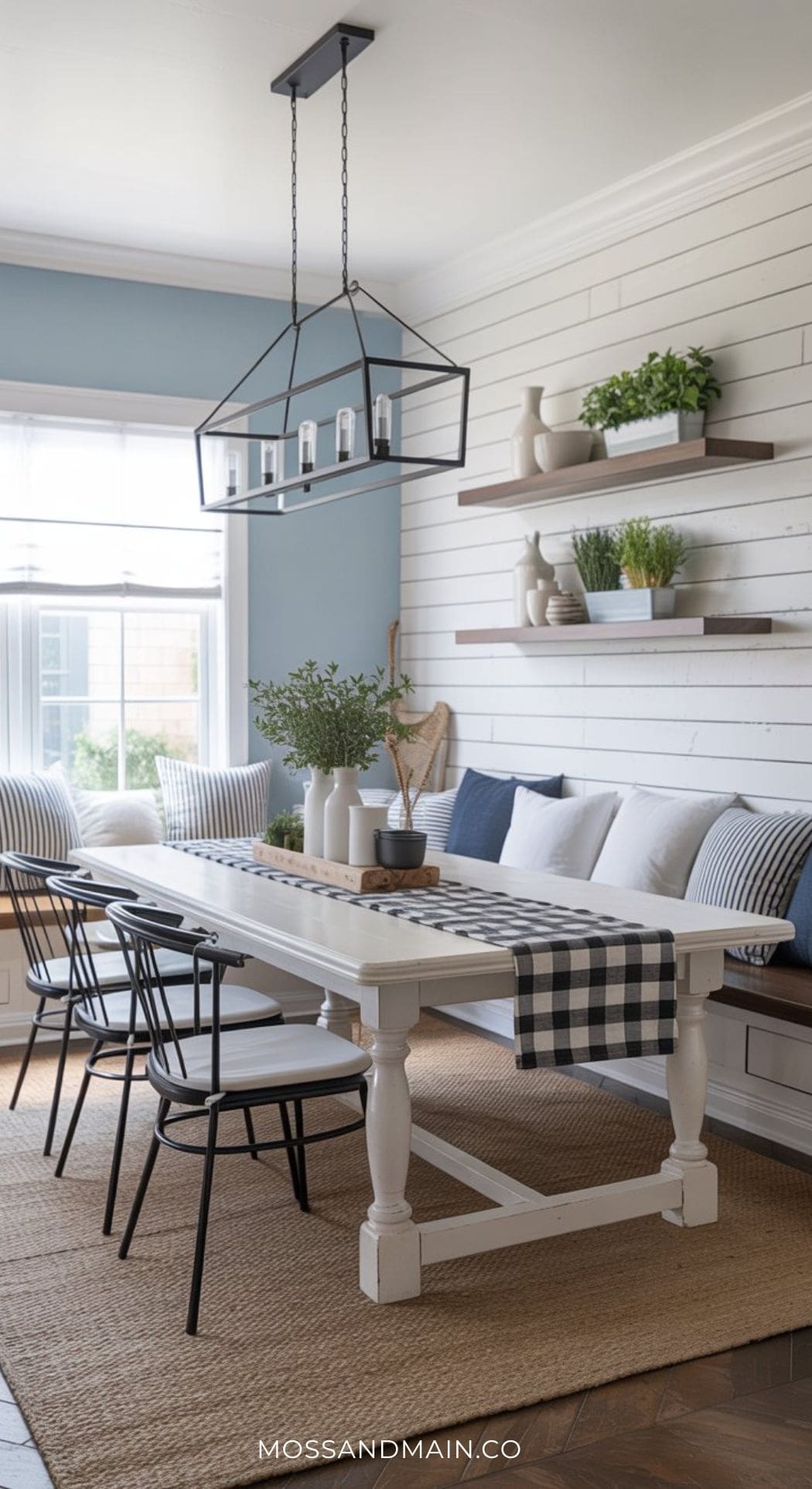Bright farmhouse dining room with a white table, black chairs, built-in bench seating, shiplap walls, and floating shelves with plants. For more inspiration, discover Blue Dining Room Ideas in our Dining Room Guide.