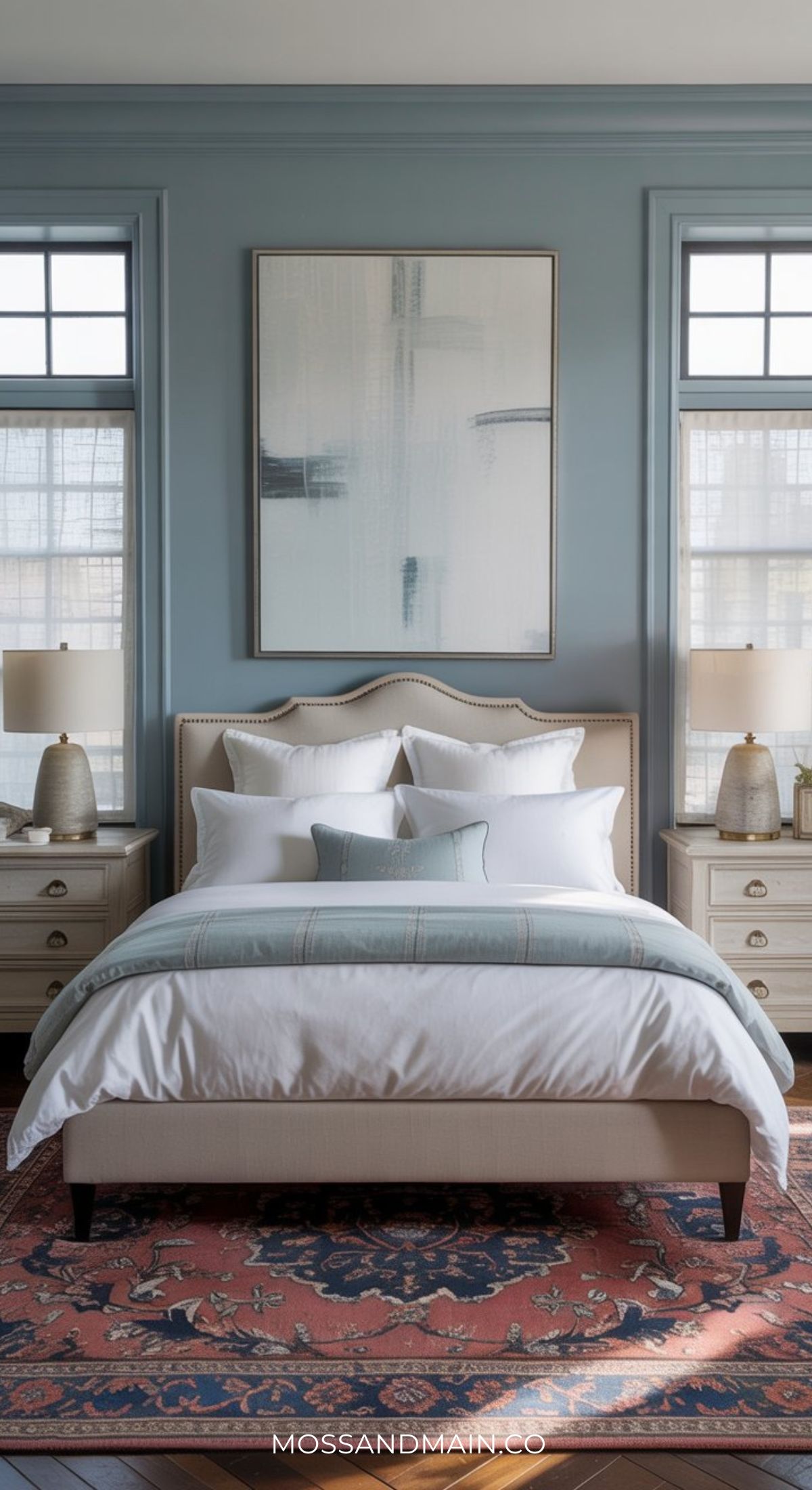 A stylish bedroom with a grey upholstered bed, white bedding, blue accent pillow, and ornate red and blue rug offers elegant bedroom inspiration for those seeking fresh bedroom ideas with a touch of sophistication.