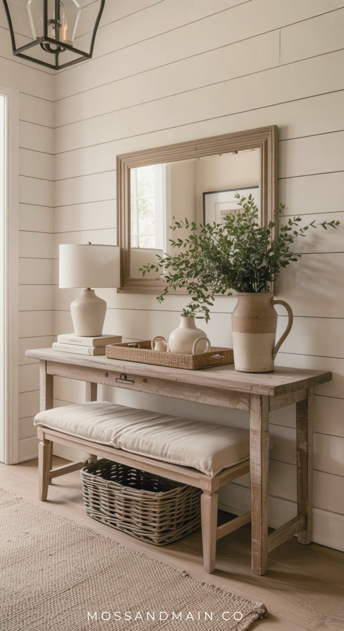 A warm entryway with a wooden console table, a bench with a wicker basket underneath, pottery decor, and a mirror on a white shiplap wall—perfect inspiration for rustic entryway ideas.