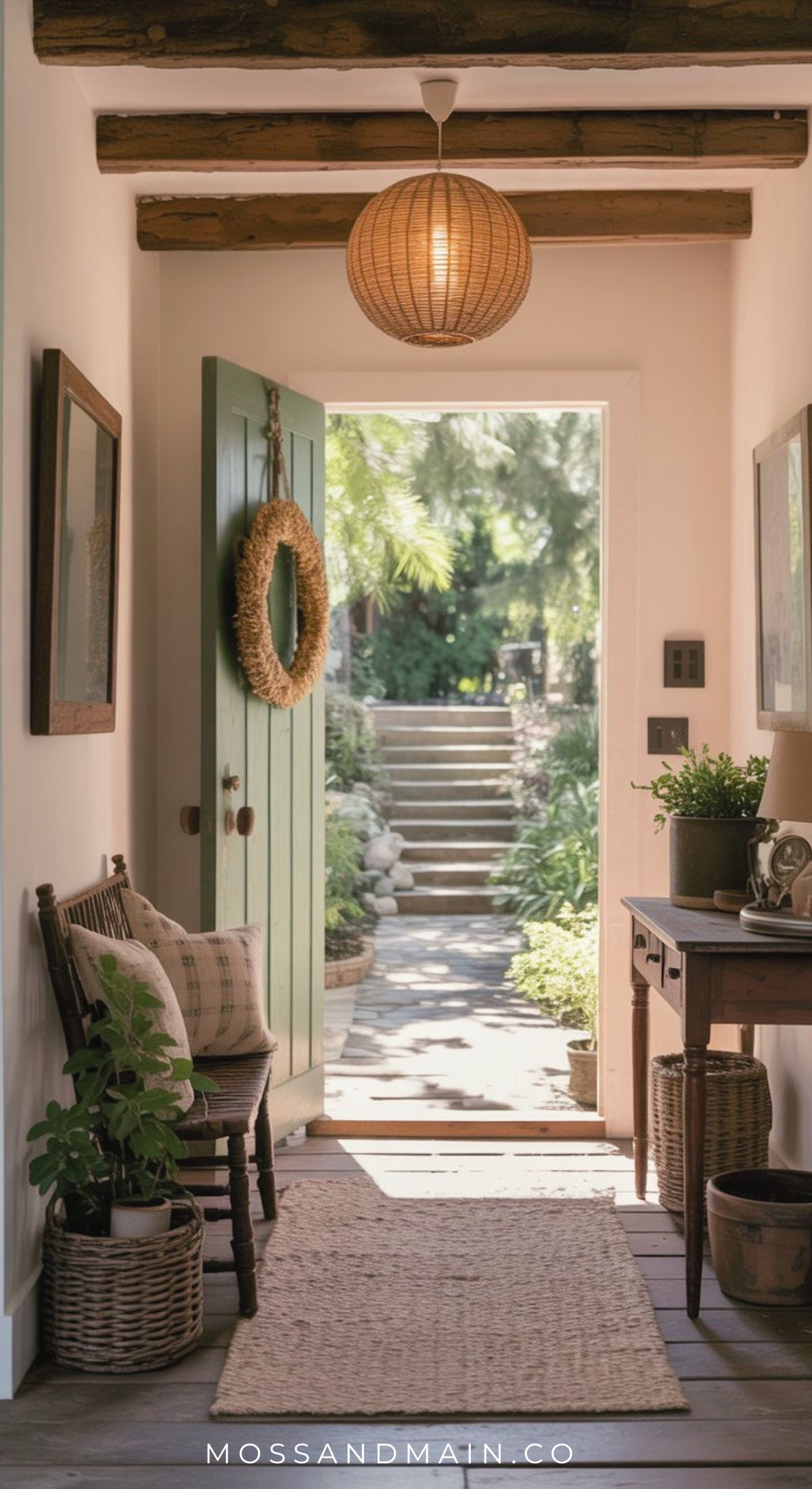 A cozy, warm entryway with a green door opens to a sunlit garden. A wooden bench with pillows, potted plants, framed art, and a woven rug create rustic entryway ideas, while a straw wreath decorates the door and natural light fills the space.