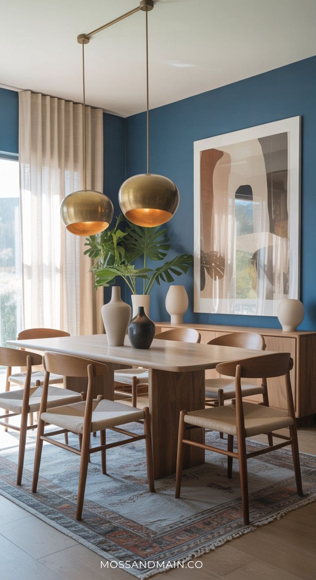 A modern blue dining room with a wooden table, six chairs, neutral vases, large abstract artwork, gold pendant lights, floor-length curtains, and a patterned rug—perfect inspiration for Blue Dining Room Ideas.