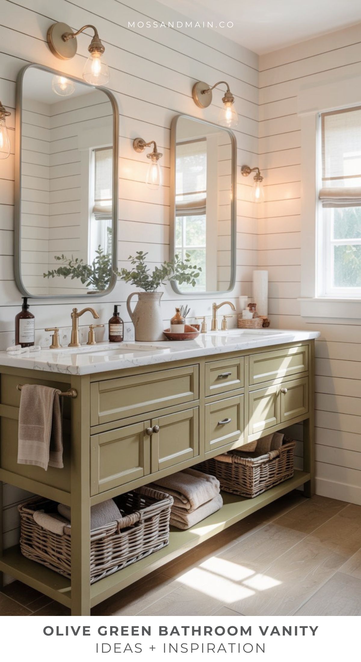 A bathroom features an olive green vanity with marble countertop, gold fixtures, twin mirrors, and wall sconces. Woven baskets are stored underneath. White shiplap walls and a window bring in natural light.